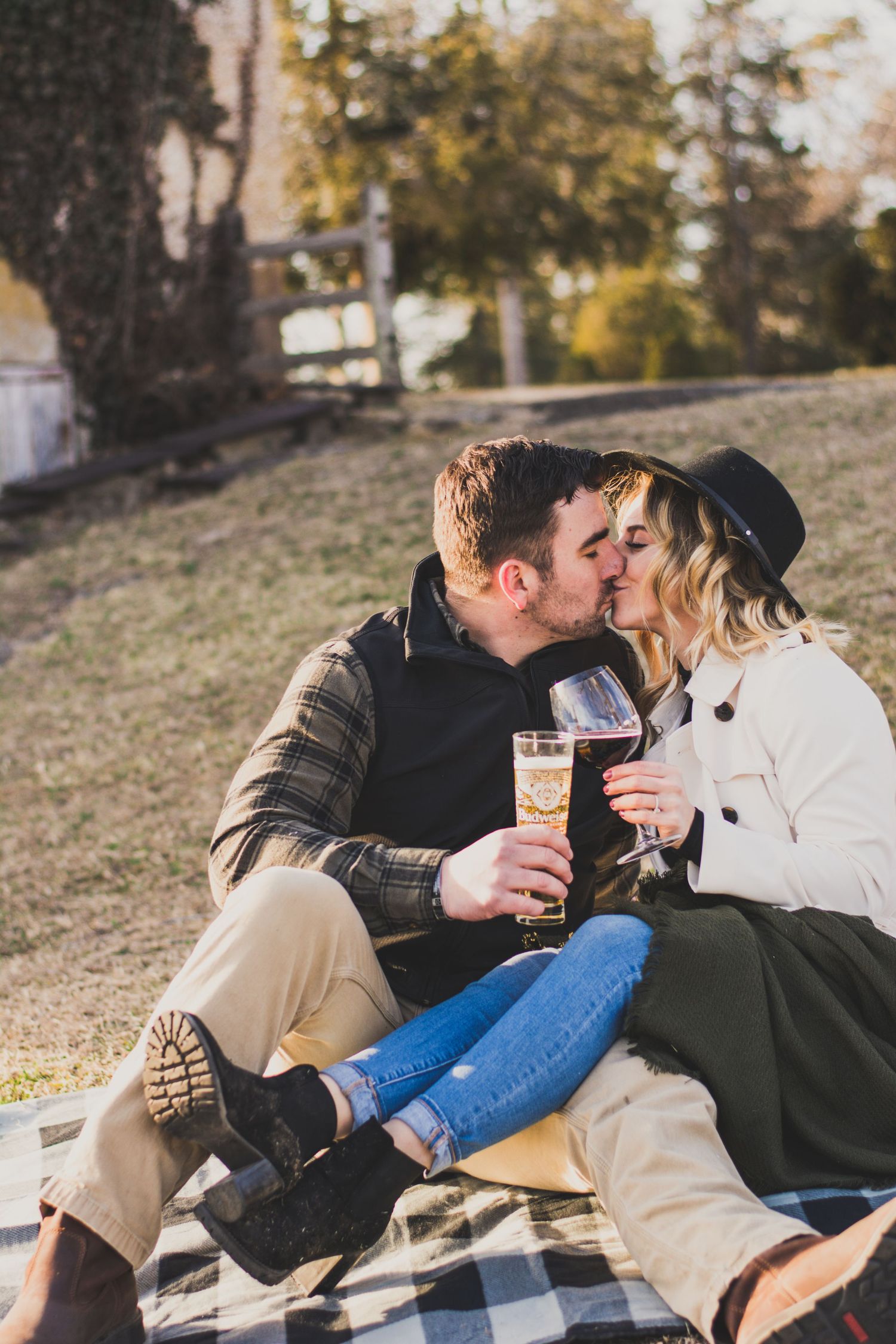 Couple sharing a kiss while holding champagne glasses during an outdoor picnic on a sunny day.