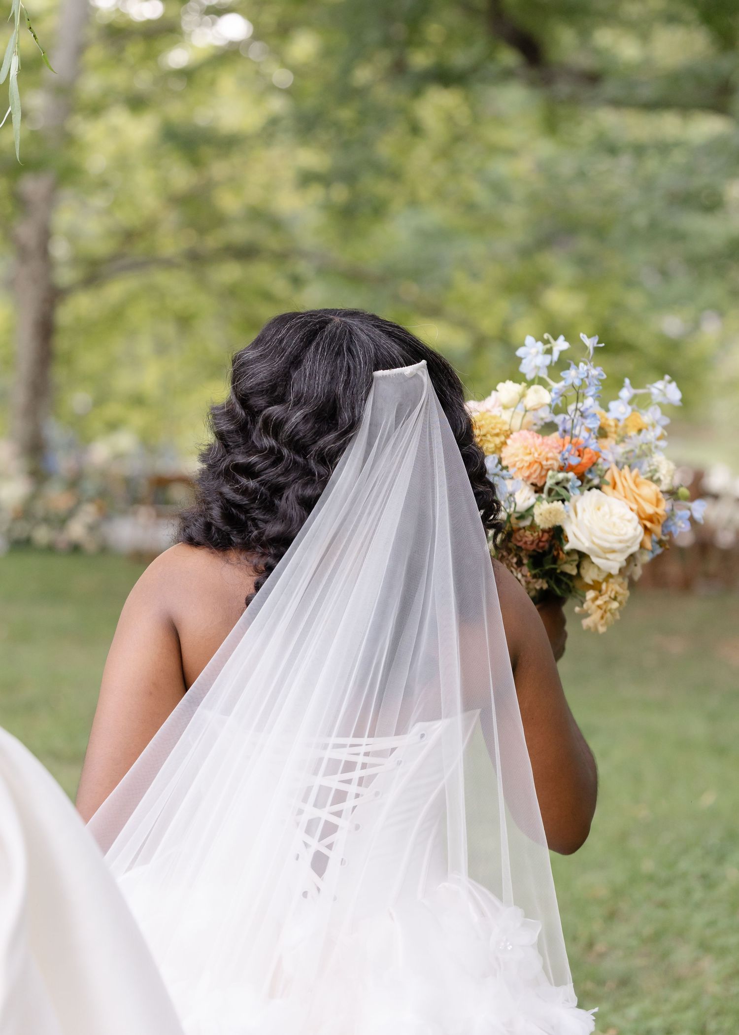 Back view of Black bride in lace corset wedding gown holding a colorful bouquet of orange, yellow, and blue flowers.