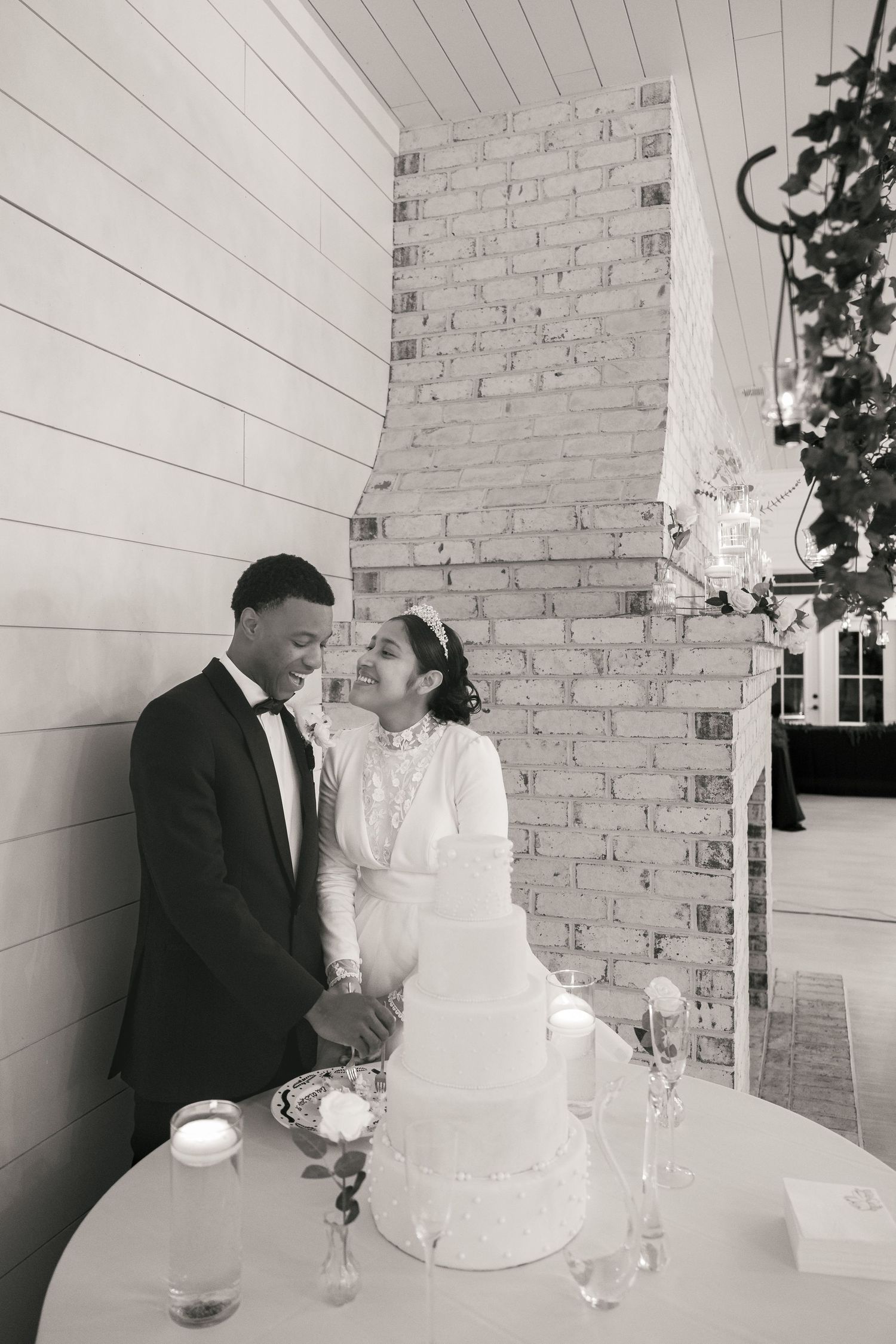Bride and groom cut white tiered wedding cake in black and white photo.