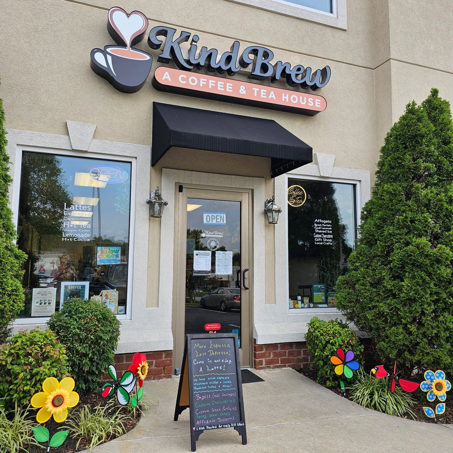 Exterior of Kind Brew Coffee & Tea House, Roanoke, VA with colorful flower decorations, chalkboard sign, and welcoming storefront entrance.
