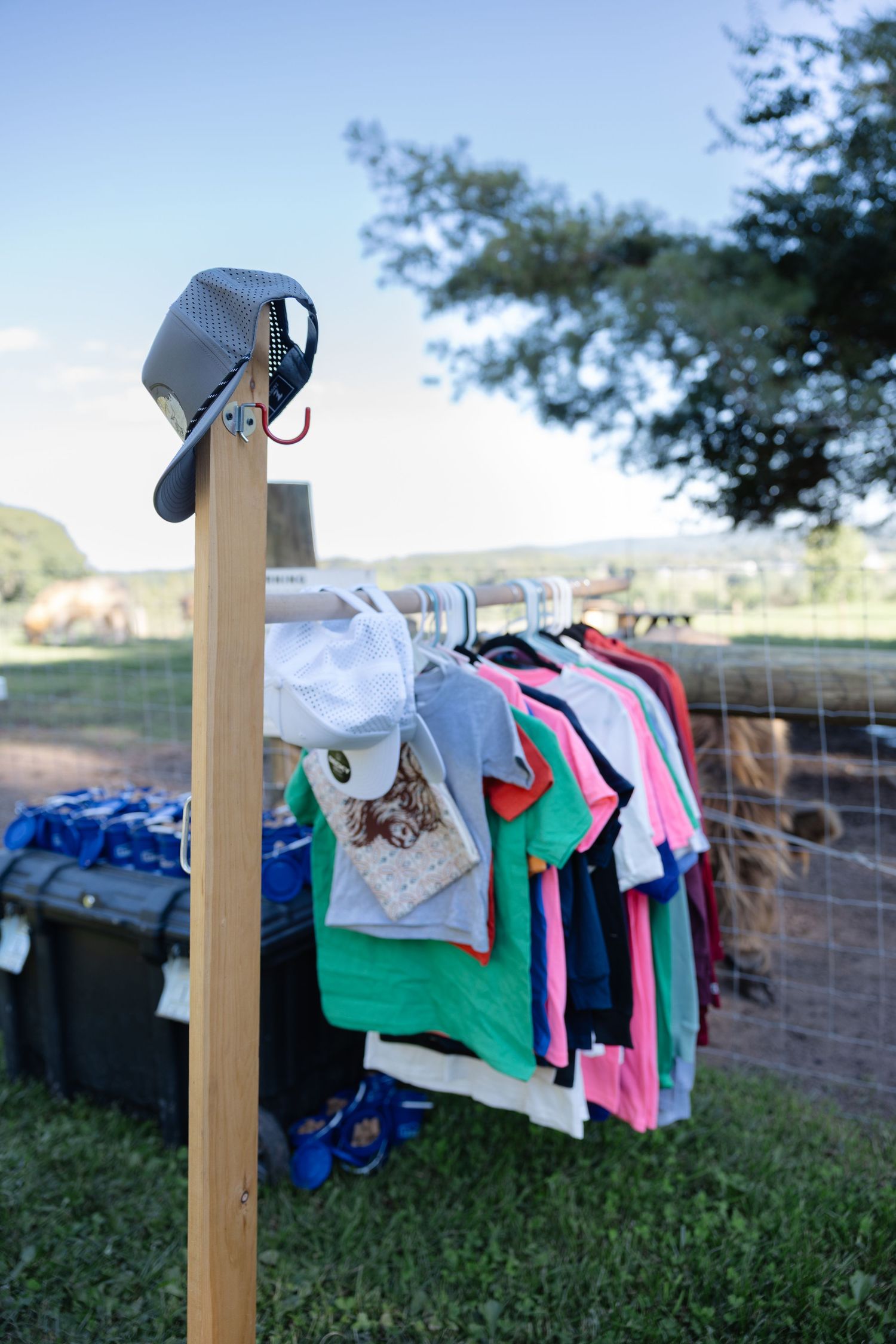 Colorful childrens clothing displayed on an outdoor rack at a farm petting zoo event on a sunny day.