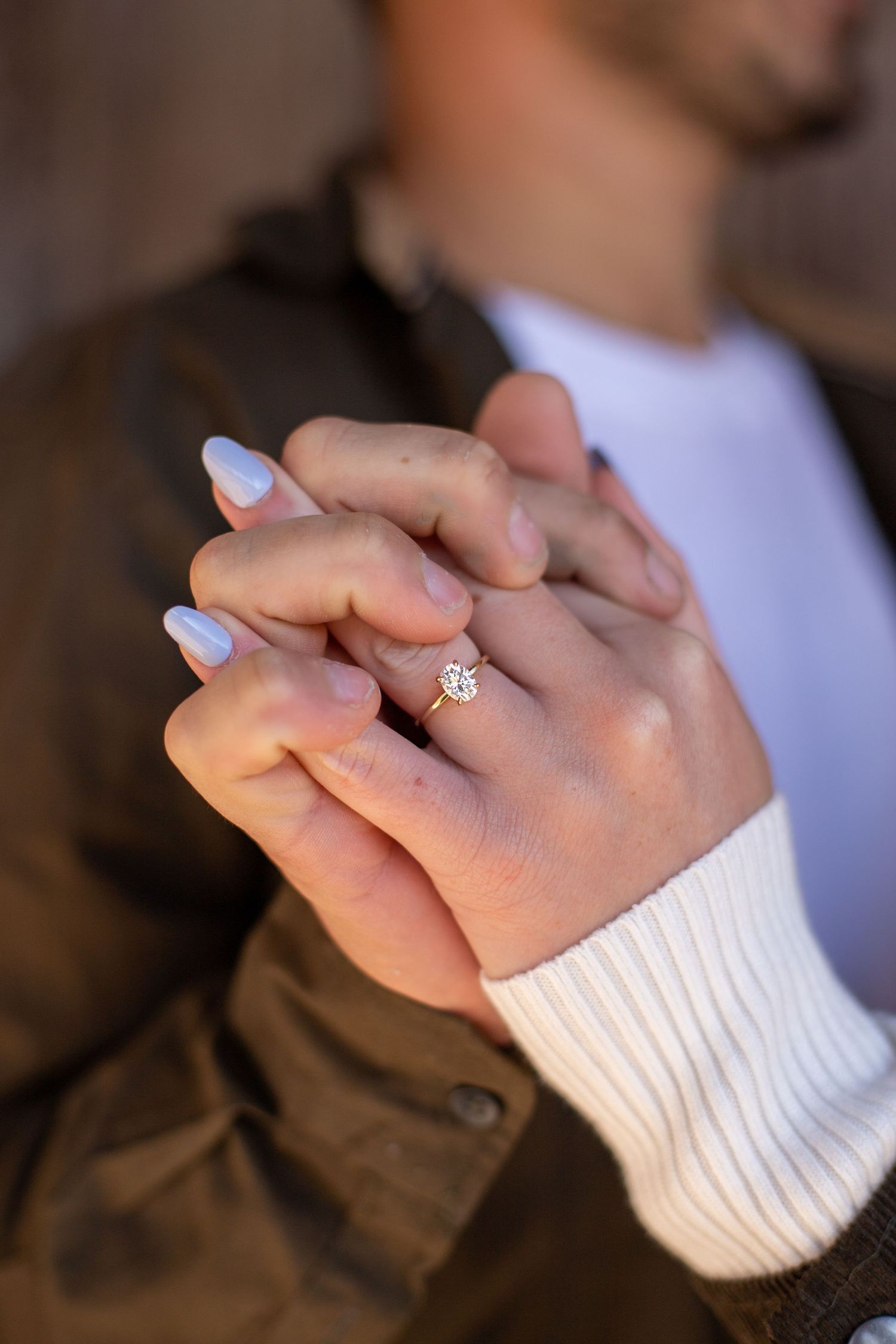 Close-up of engaged couple holding hands showing a diamond solitaire engagement ring.