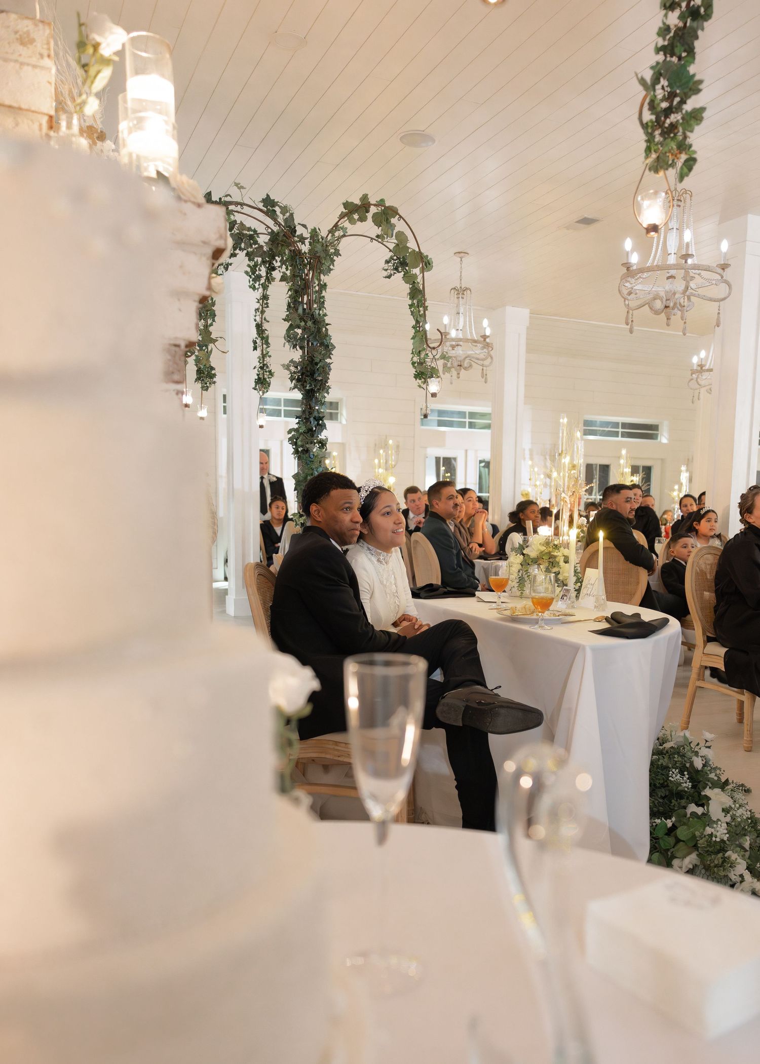 Bride and groom sit at sweetheart table during elegant barn wedding reception.