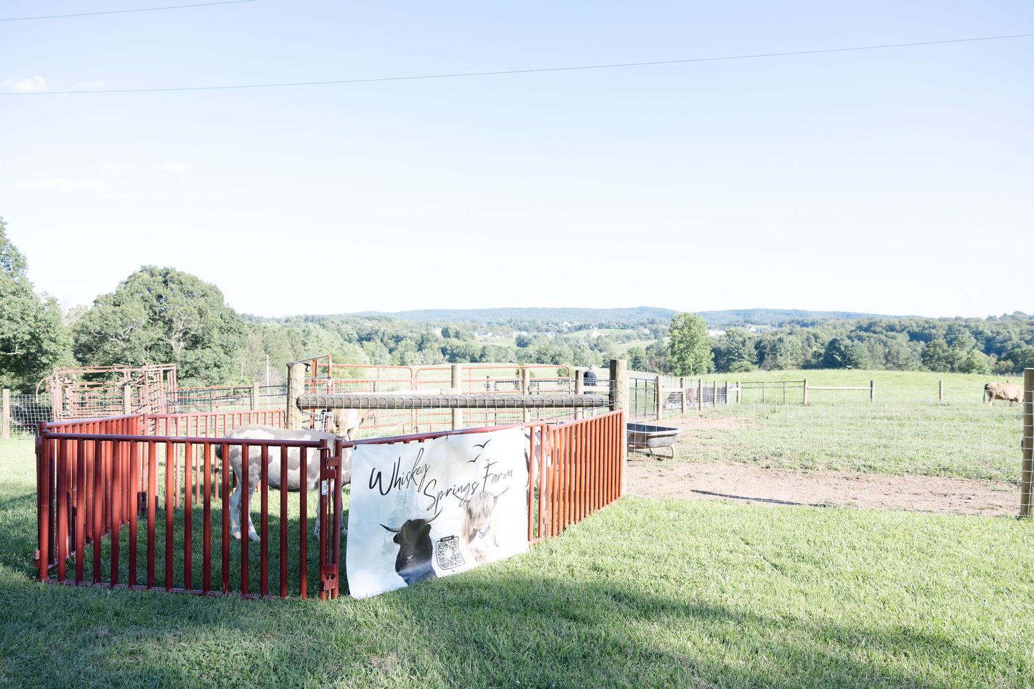 Red circular livestock pen on a green farm with rolling hills and open pasture visible in the background.