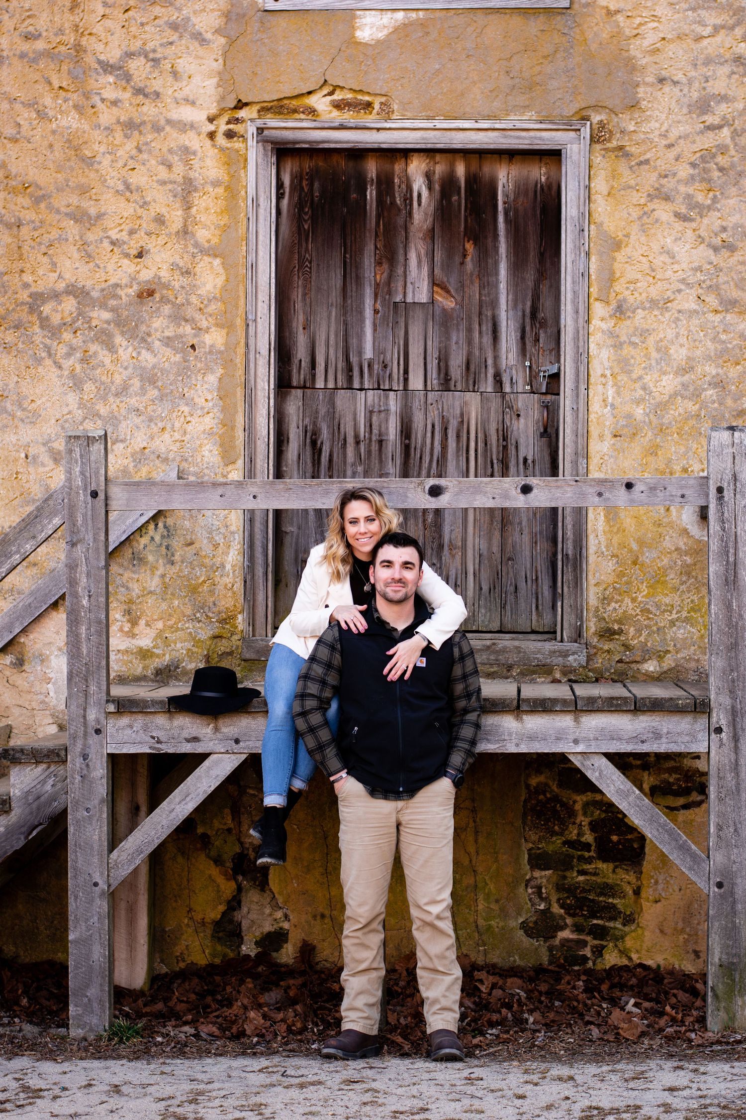 Couple posing together on wooden steps in front of a weathered stone building with vintage door.