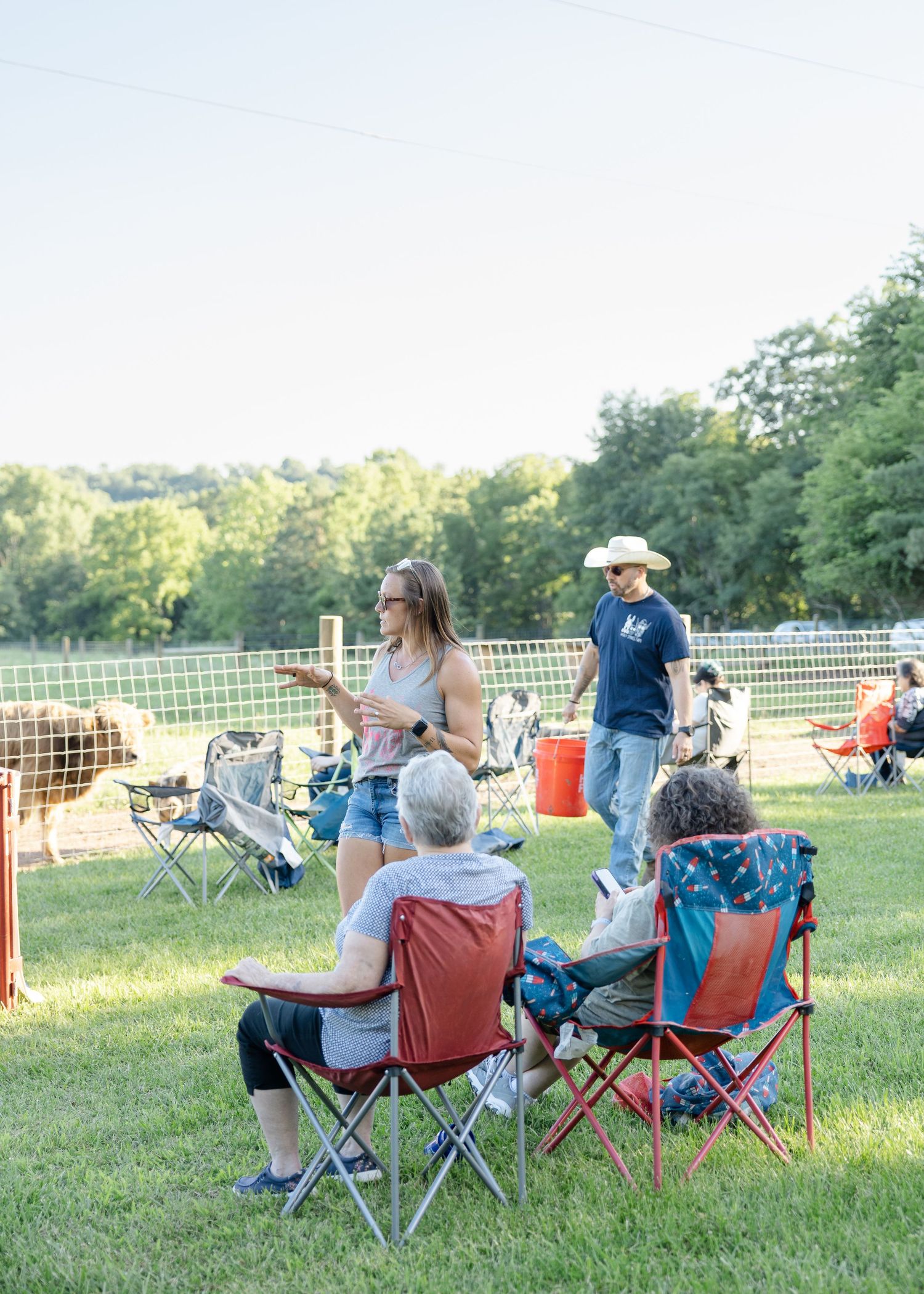 People relaxing in folding chairs on green grass at an outdoor farm event on a sunny day.