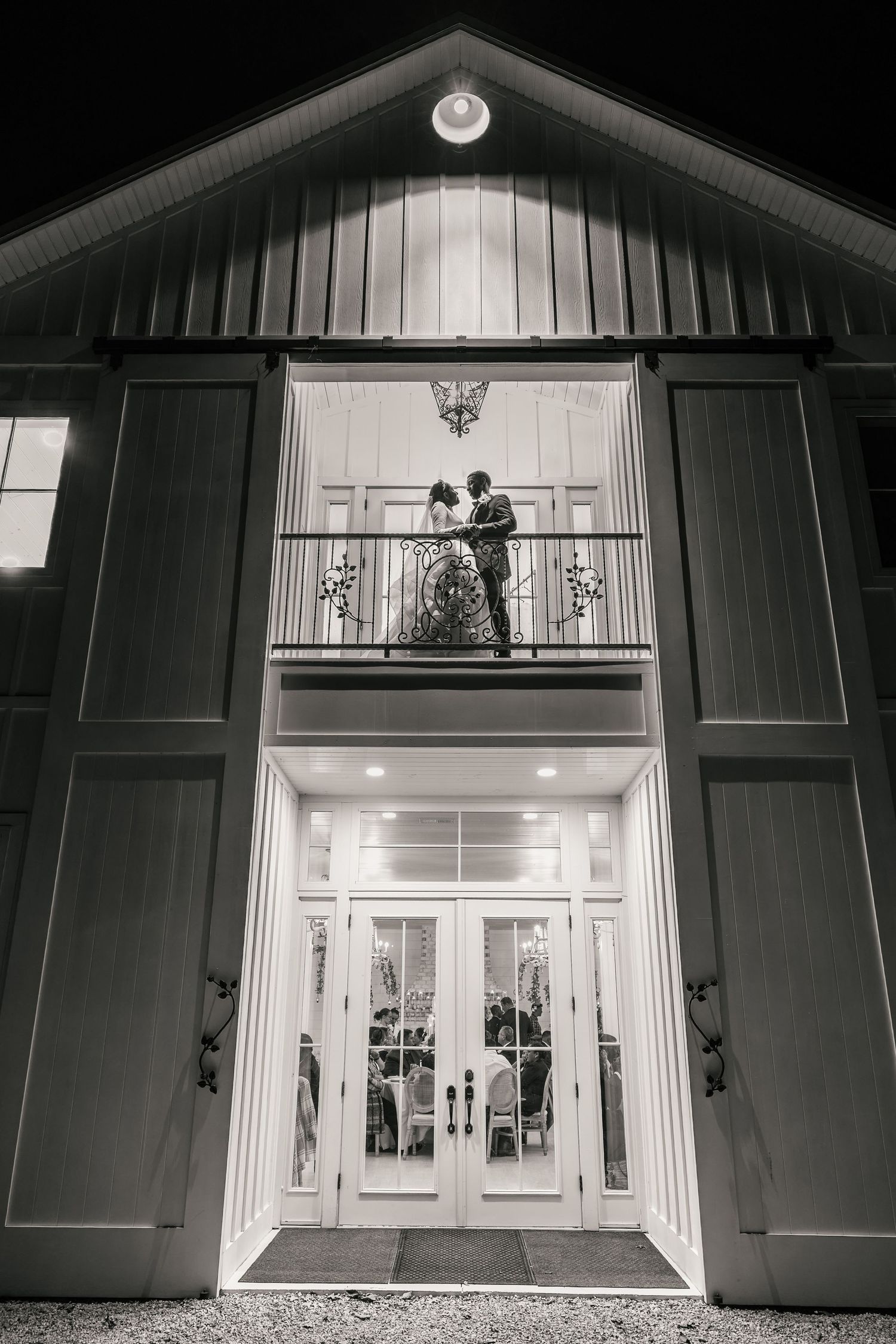 Black and white photo of a couple sharing a romantic moment on a barn venue balcony at night.