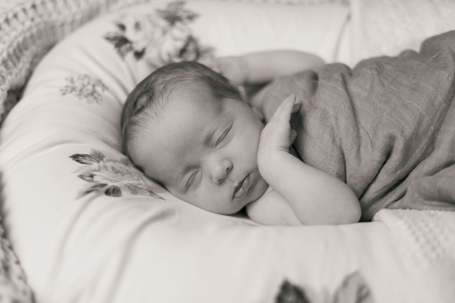 Peaceful newborn baby sleeping wrapped in a soft blanket in a black and white portrait.