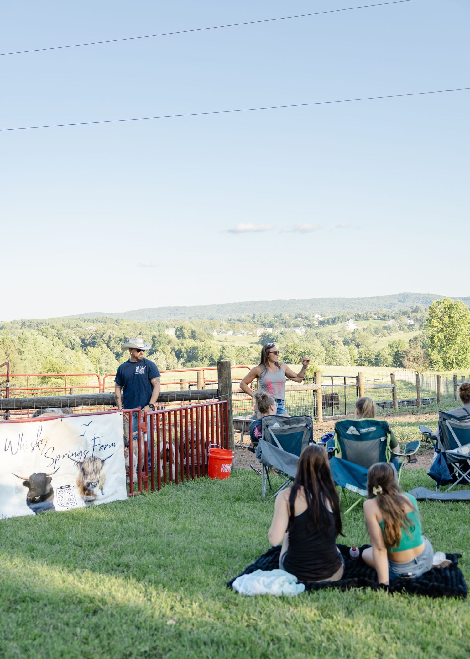 Group of visitors relaxing on grass while attending an outdoor farm animal educational event at sunset.