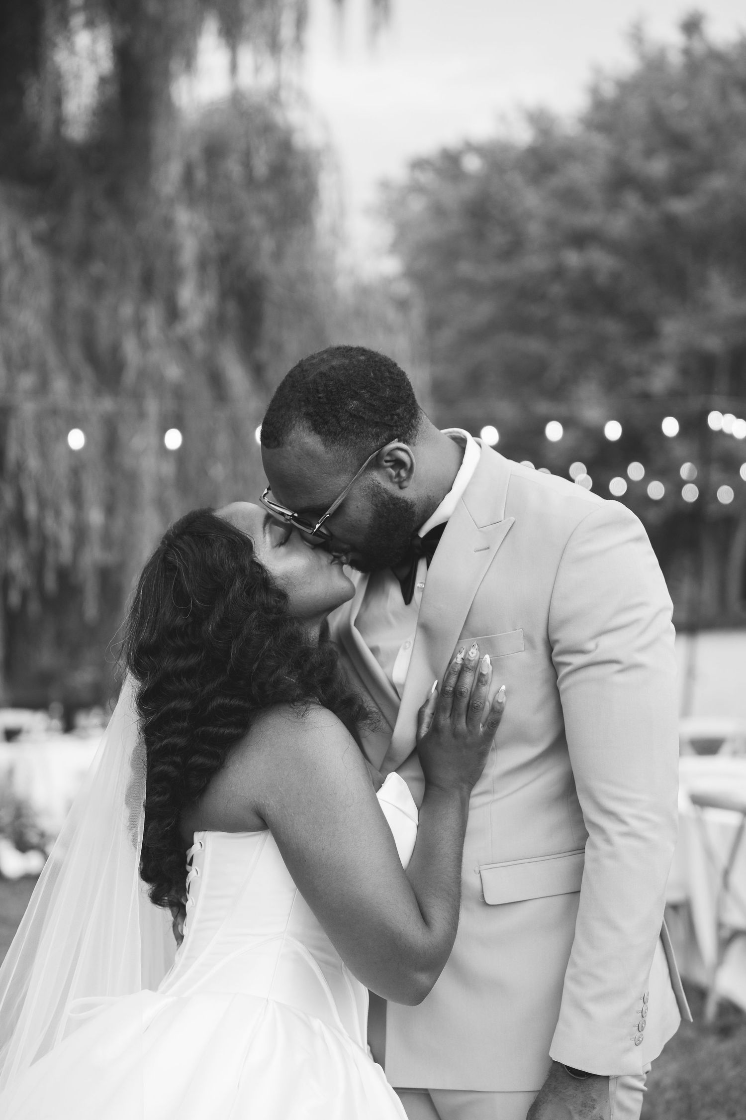 Black and white photo of a bride and groom sharing a kiss outdoors at their wedding reception.