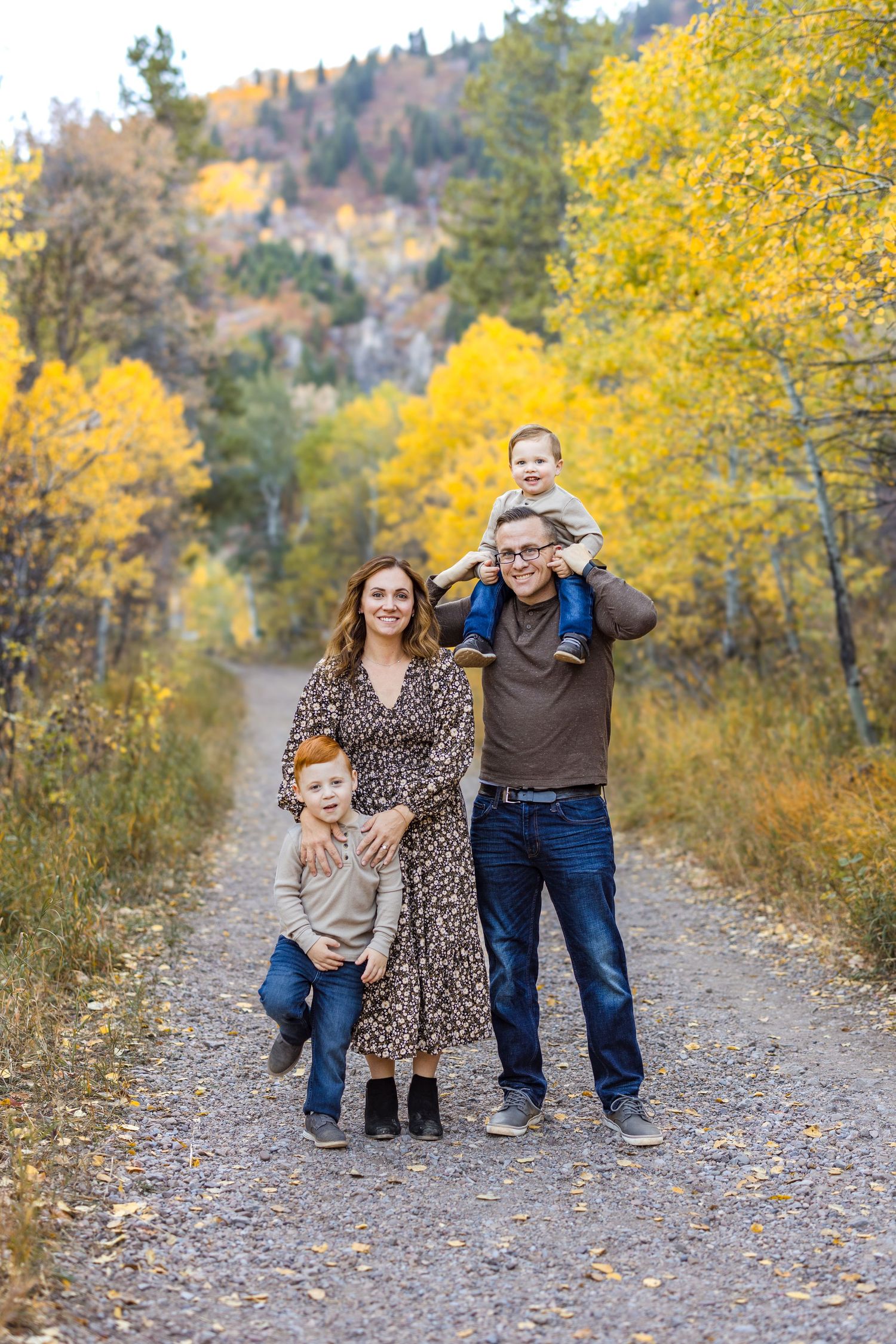 Family of four posing on a gravel path surrounded by golden autumn aspen trees.