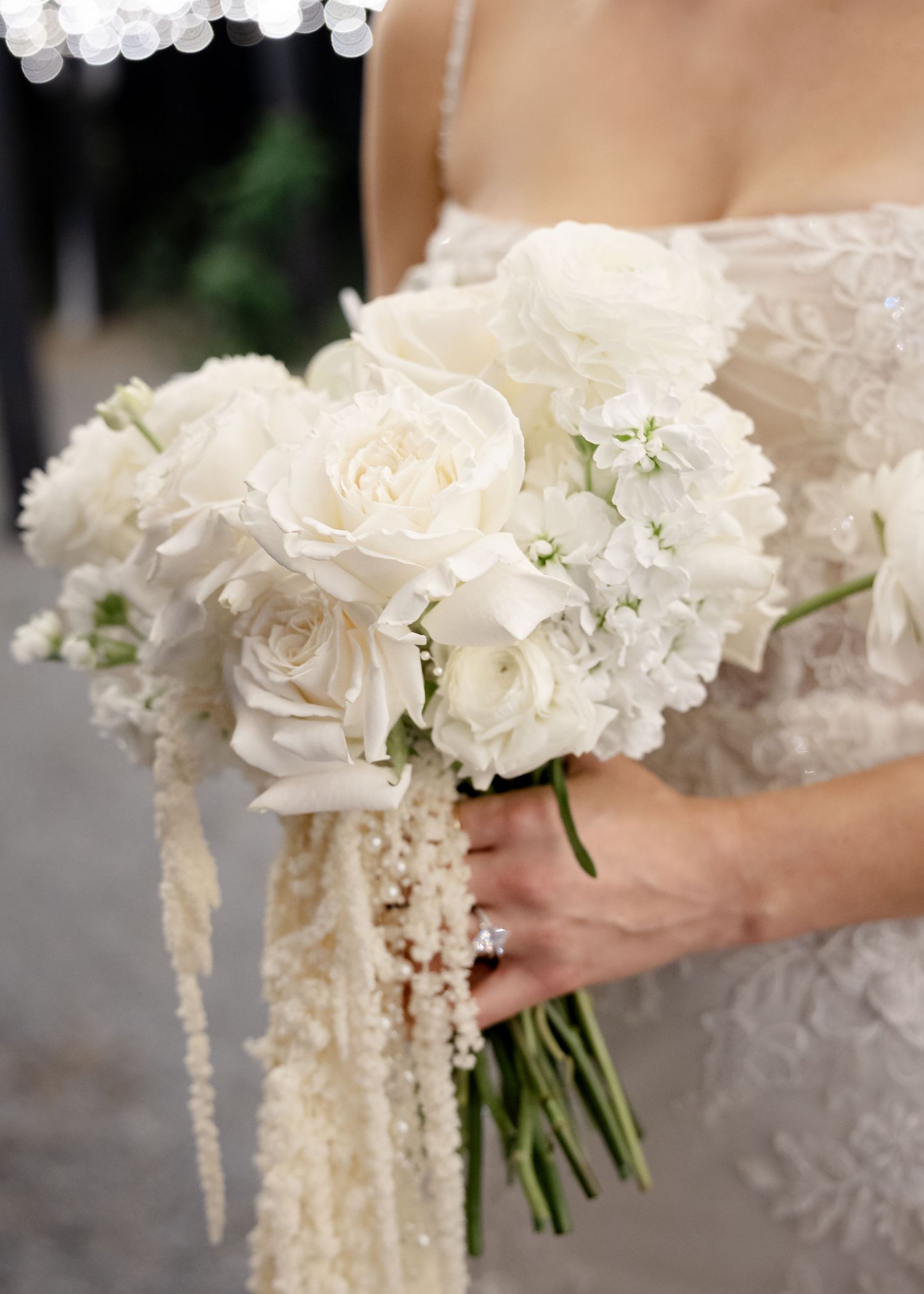Bride holding an all-white wedding bouquet featuring roses, peonies, and cascading amaranthus blooms.
