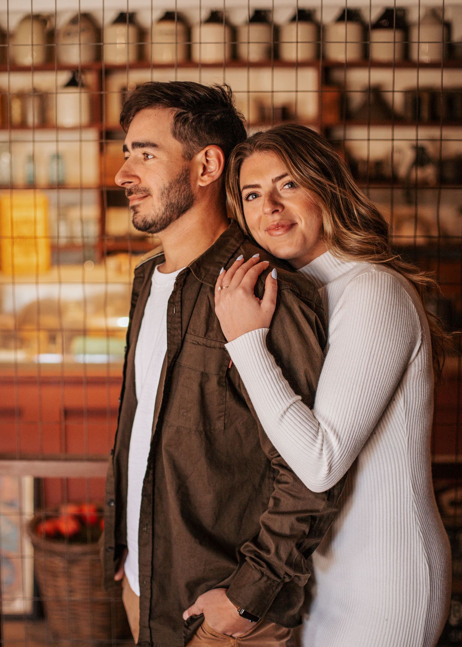 Couple posing together in a warm cafe setting, woman resting on mans shoulder.