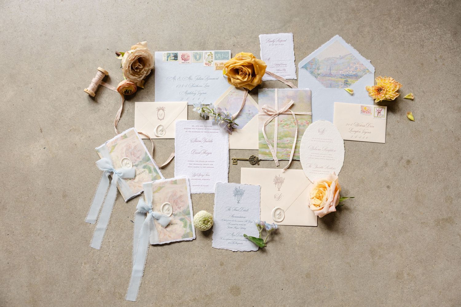 Elegant wedding invitation suite with yellow roses, blue envelopes, wax seals, and ribbon on a neutral background.