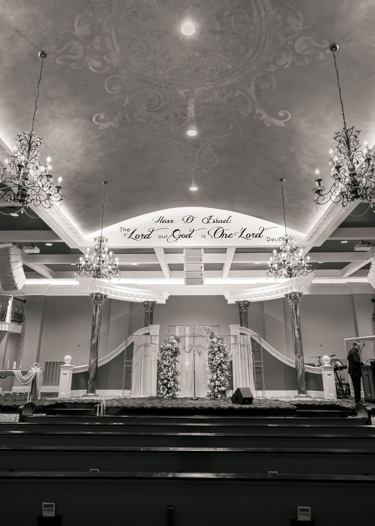 Black and white photo of elegant church interior with chandeliers and floral altar decorations.