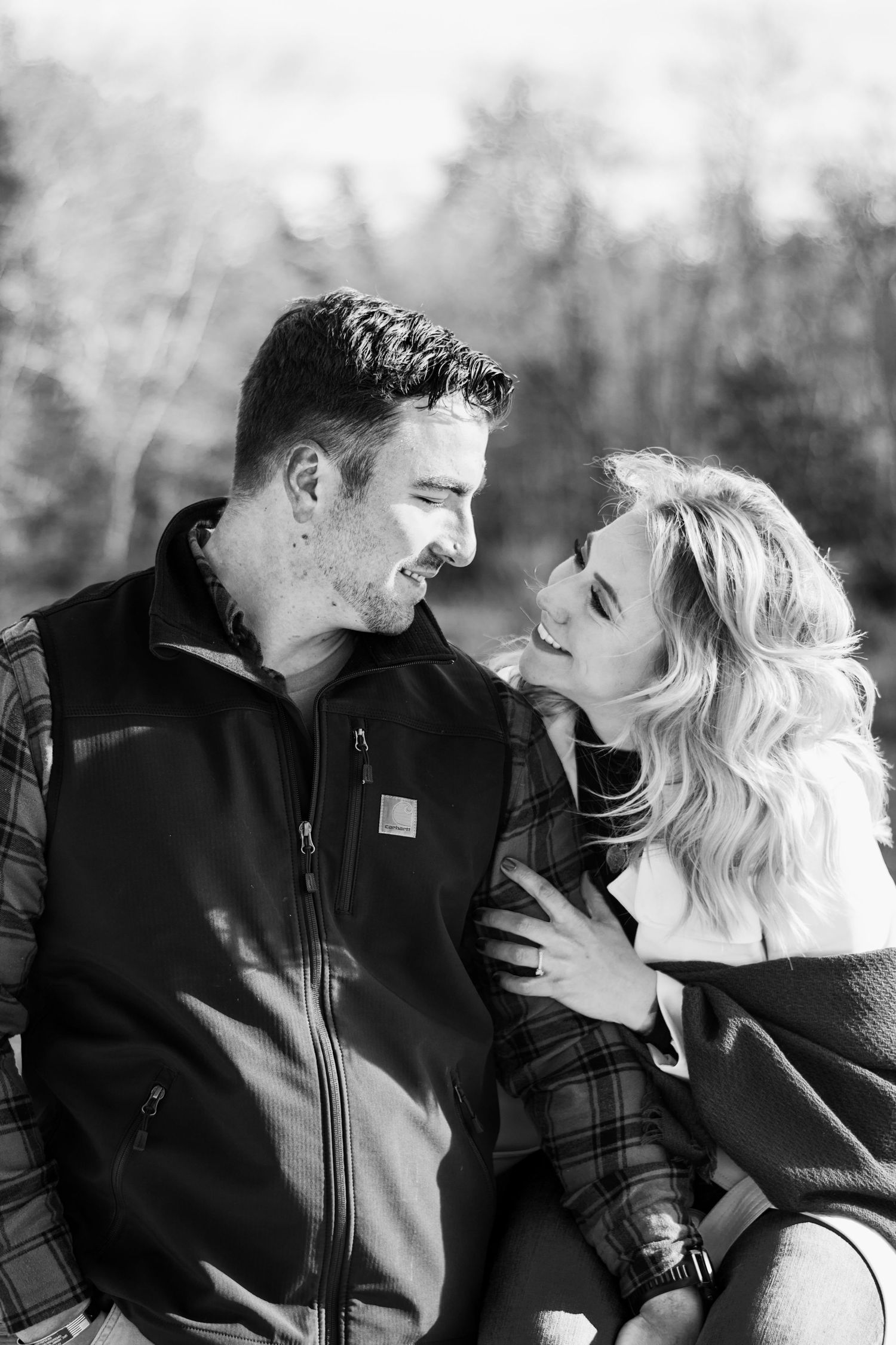 Black and white photo of a smiling couple gazing at each other outdoors, woman with blonde hair touching mans chest.