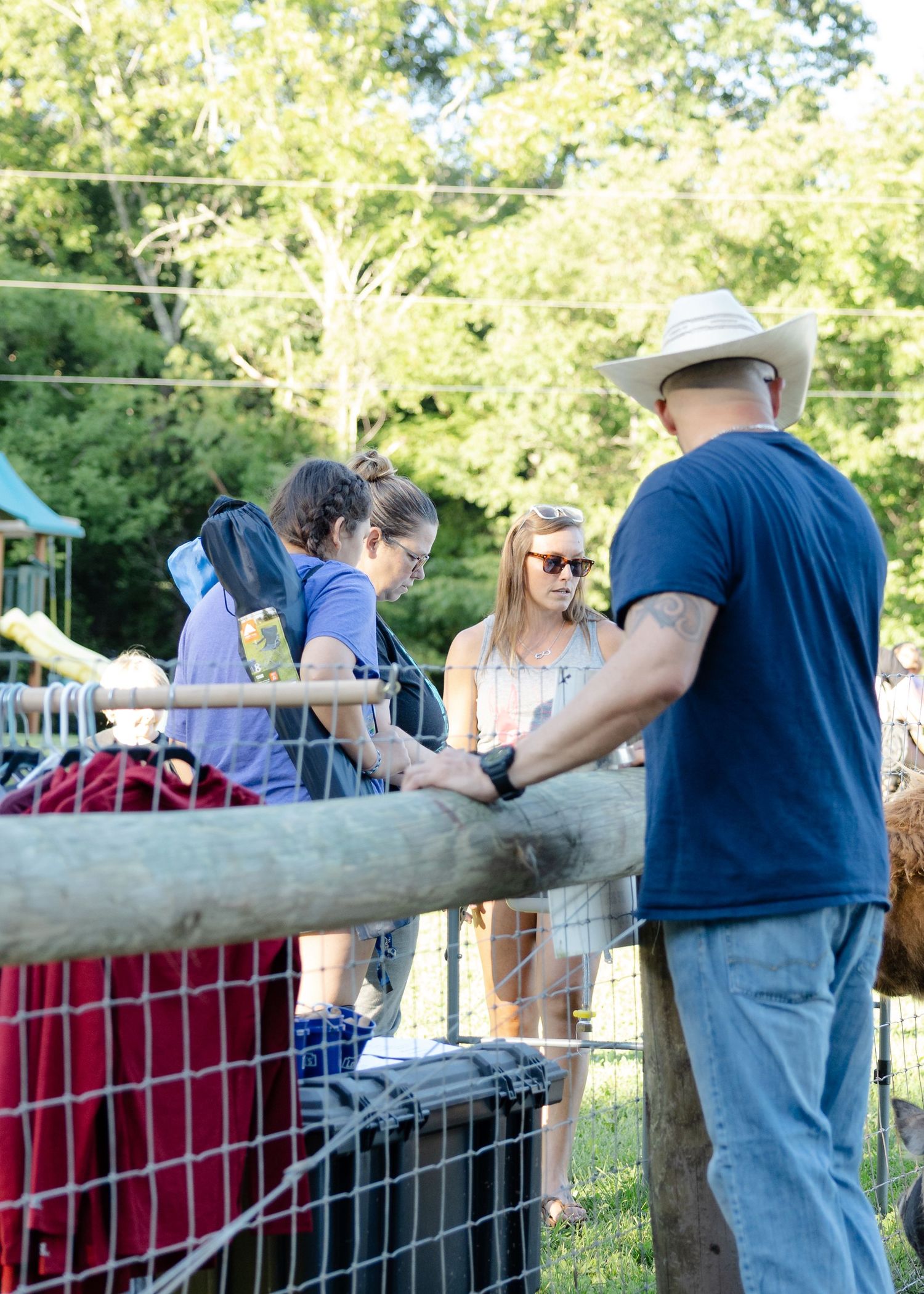 People gather at a wooden fence petting animals at an outdoor farm petting zoo on a sunny day.
