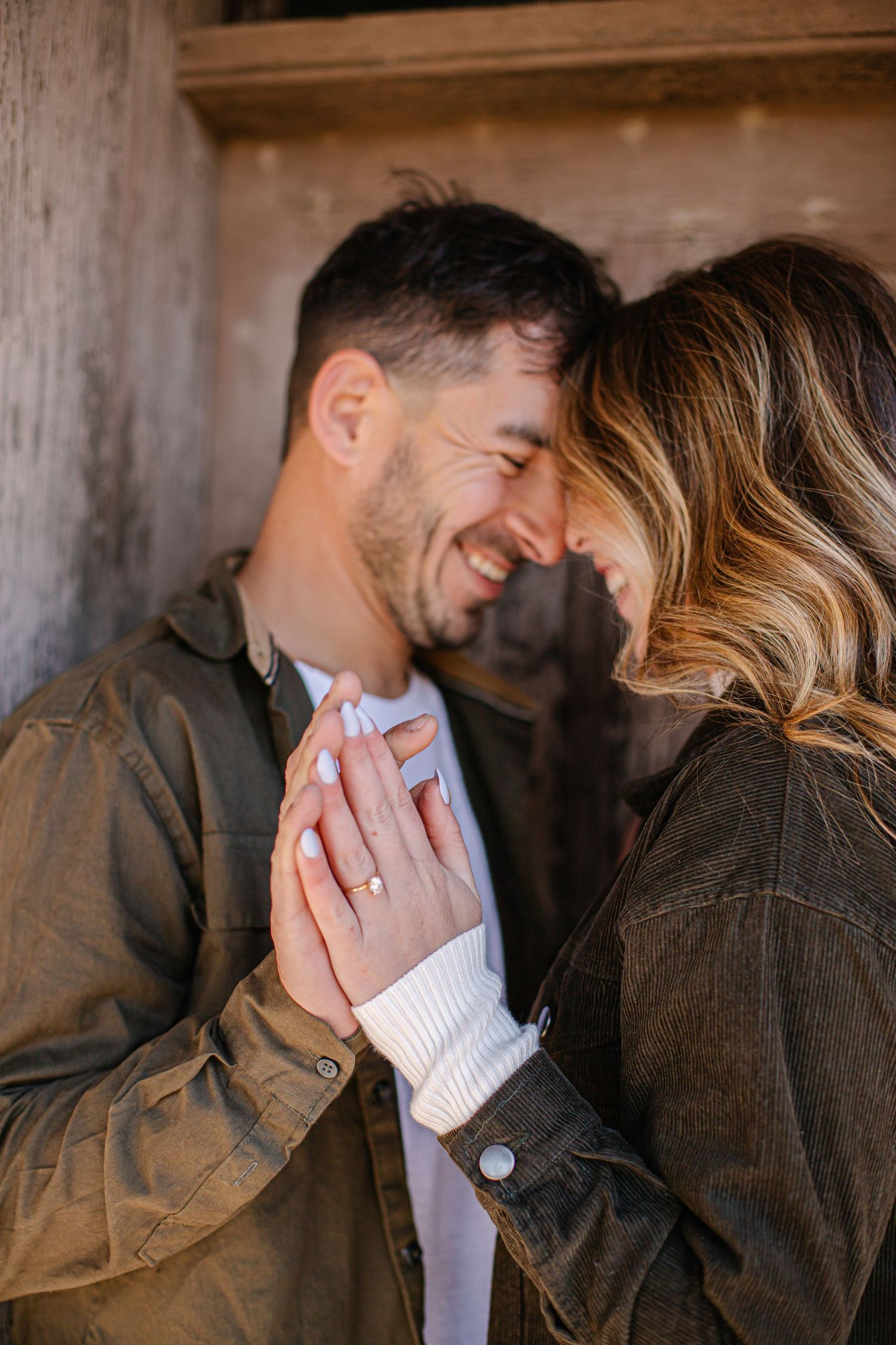 Joyful engaged couple laughing together while holding hands displaying an engagement ring.