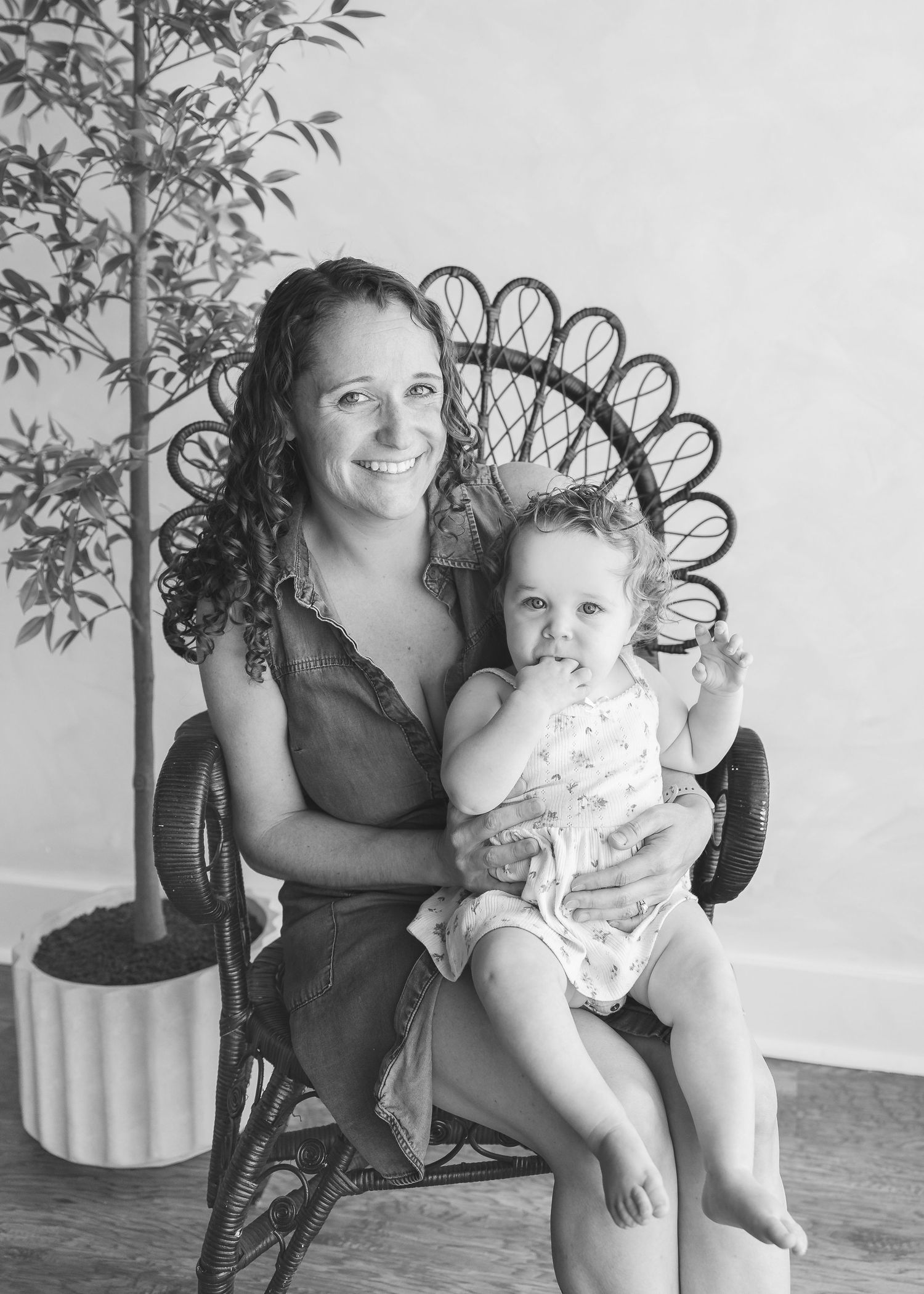 Black and white photo of a smiling mother holding her toddler in a decorative peacock chair.