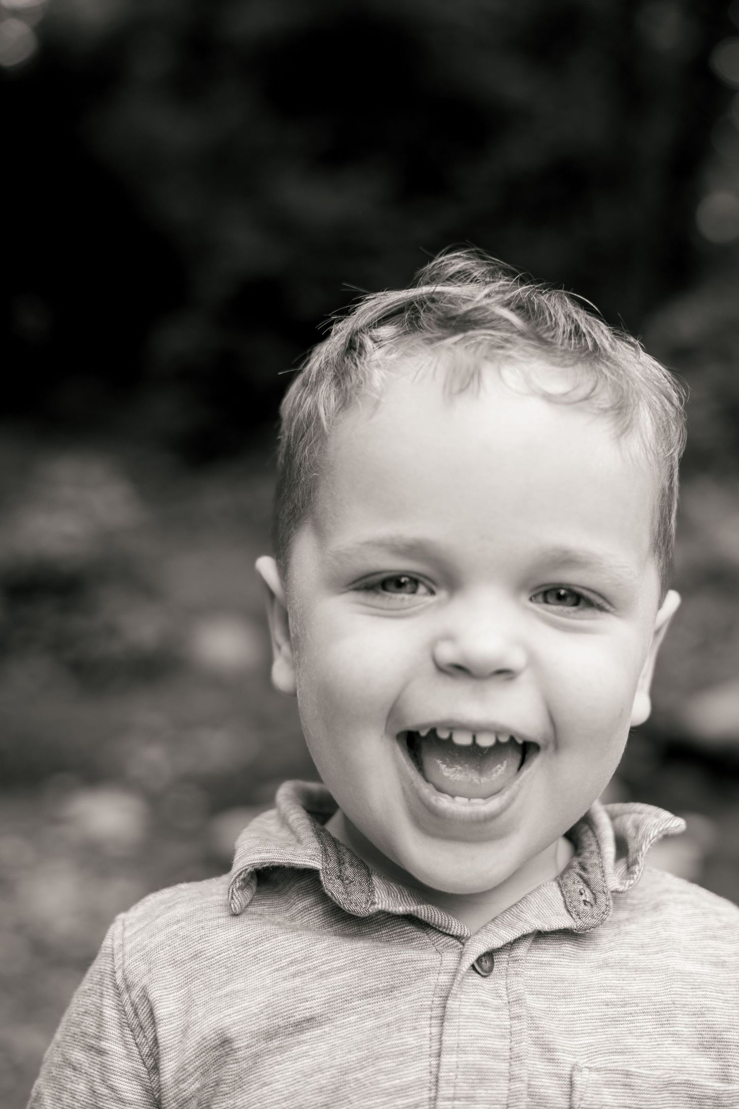 Black and white portrait of a joyful young boy laughing outdoors, wearing a collared shirt.
