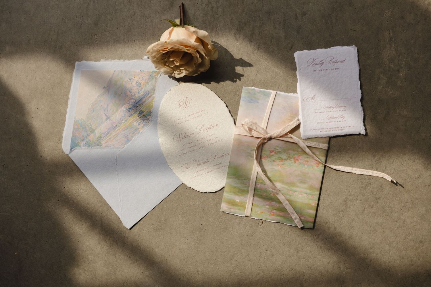 Minimalist wedding stationery flat lay with watercolor details, ribbon, and a single dried rose.