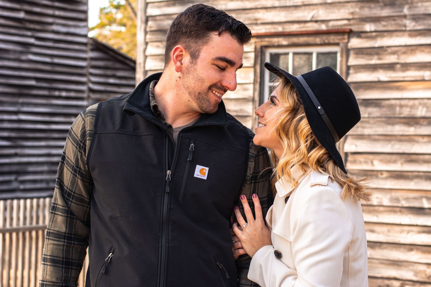 Romantic couple gazing into each other's eyes near a rustic wooden barn in autumn.