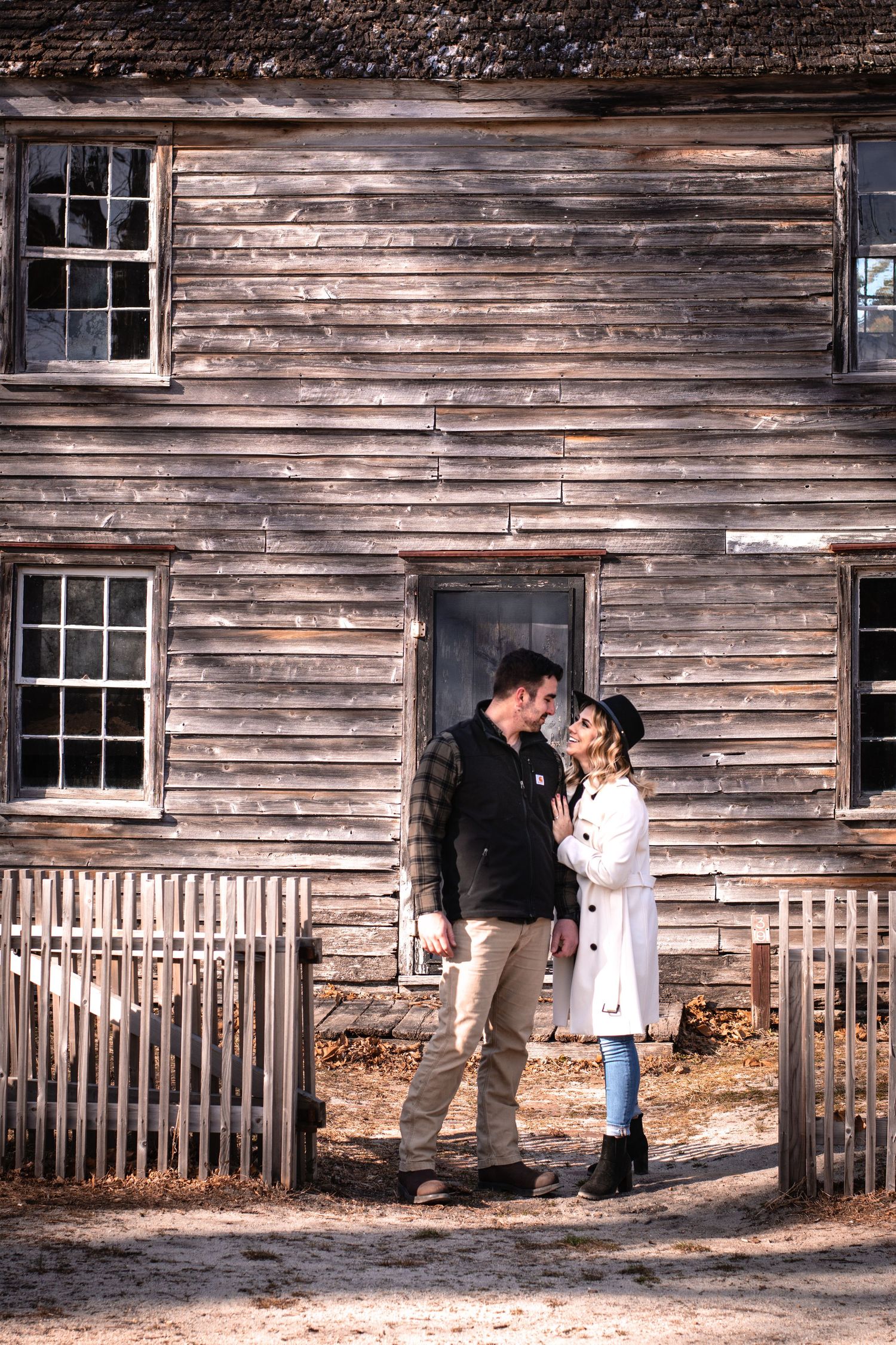 Romantic couple standing together in front of a rustic weathered wooden building during autumn.