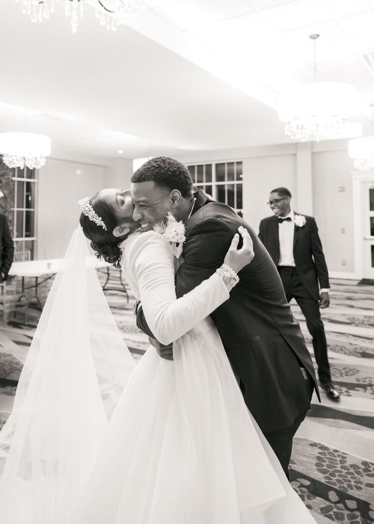 Black and white photo of a bride and groom sharing a joyful embrace at their elegant wedding reception.