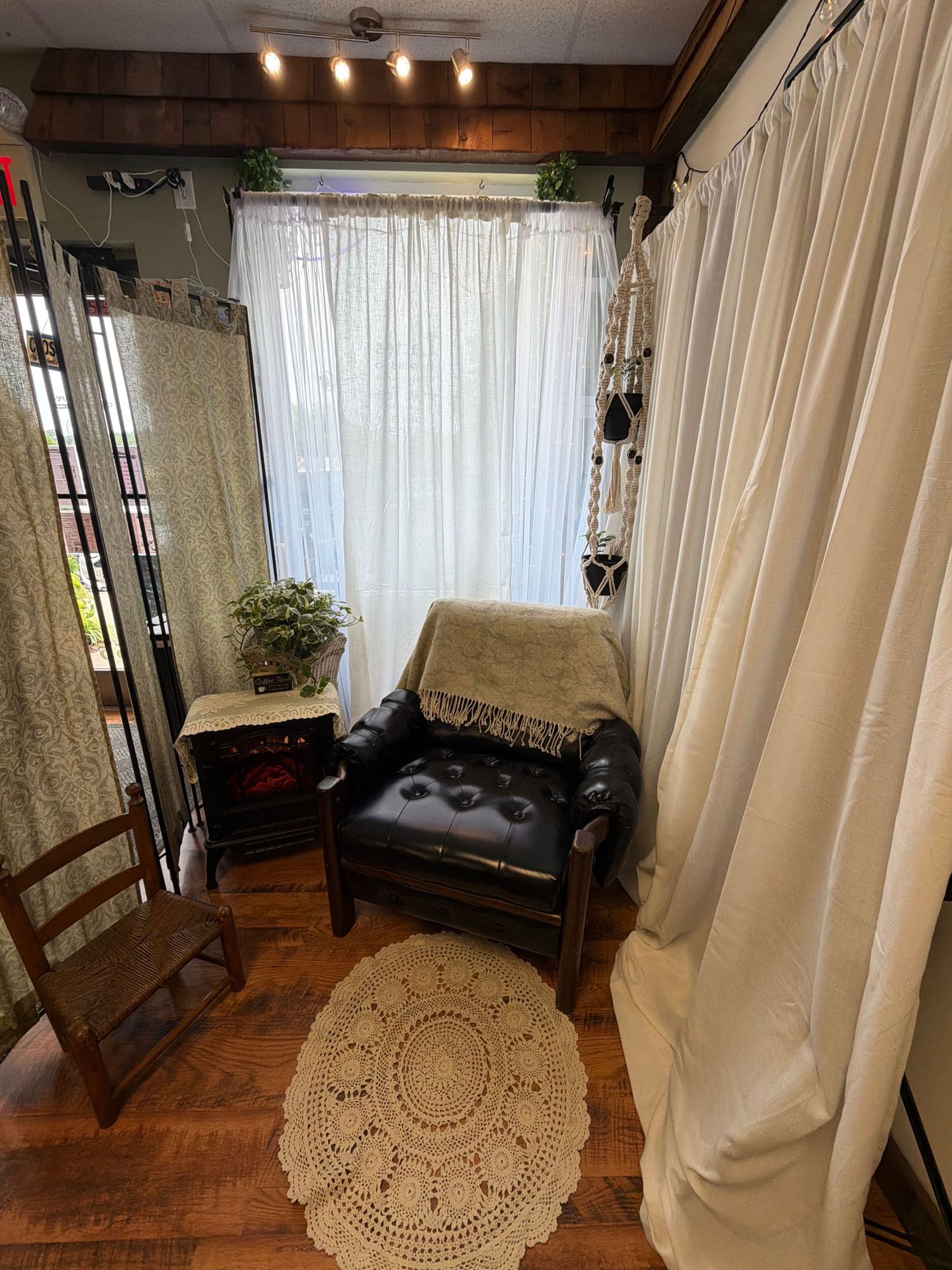 Cozy reading nook with black leather chair, crochet rug, white curtains, and wood floors in a bohemian-style room.