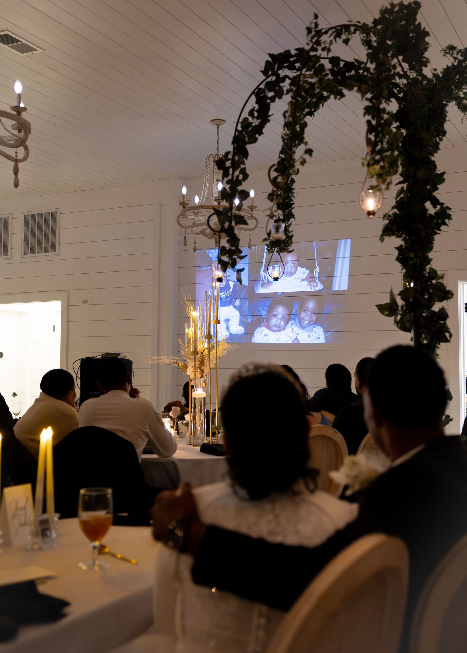 Wedding guests watch slideshow projection at romantic candlelit barn reception venue.