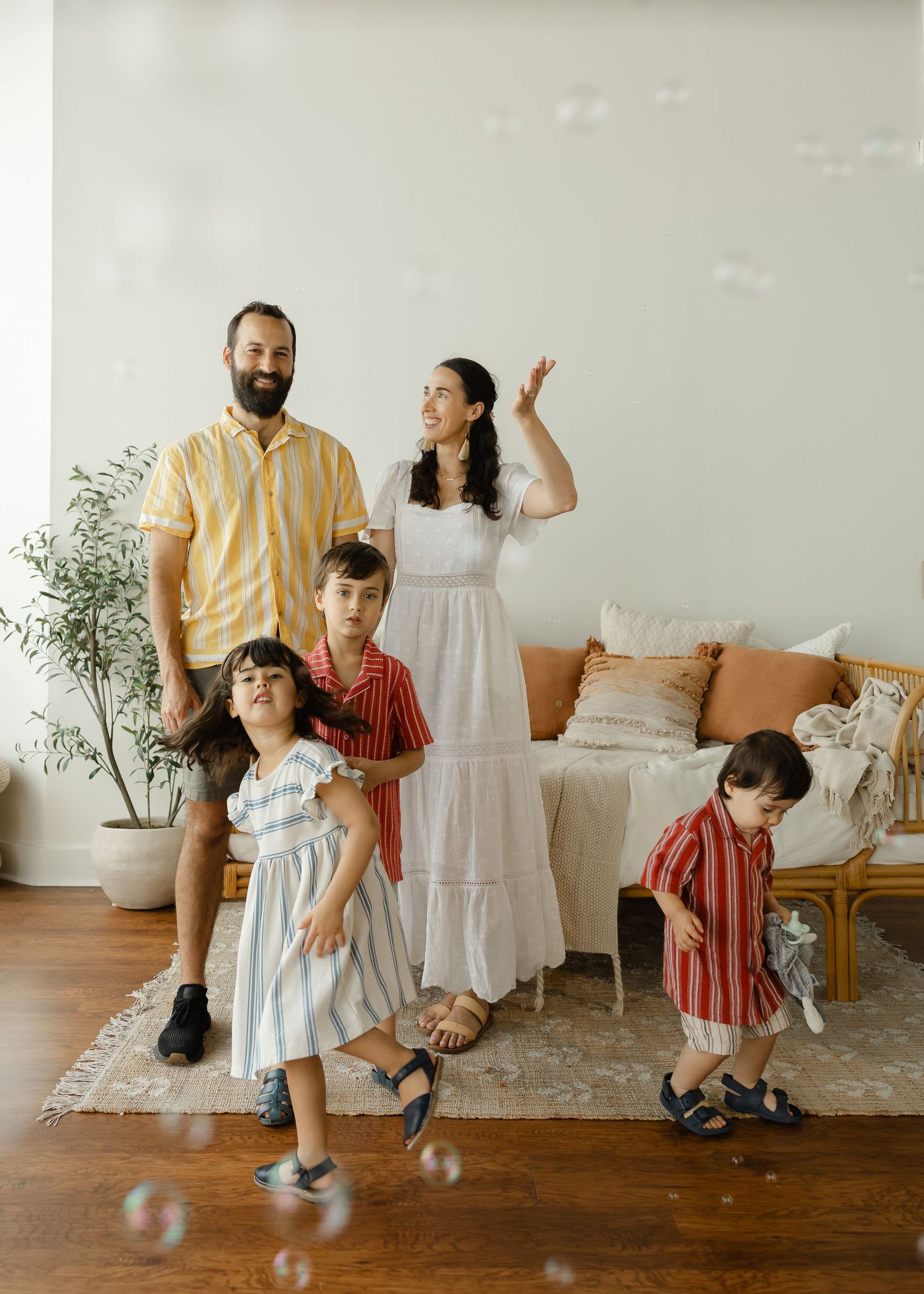 Family of five with three young children playing with bubbles in a bright white living room.