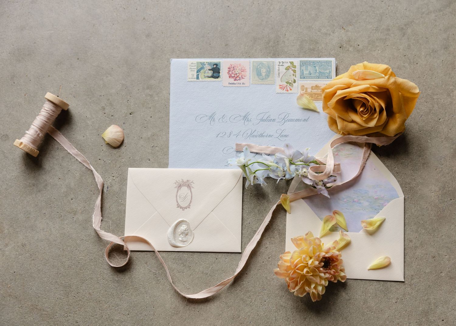 Wedding invitation suite with wax seal envelope, yellow rose, vintage stamps, and dried flowers.