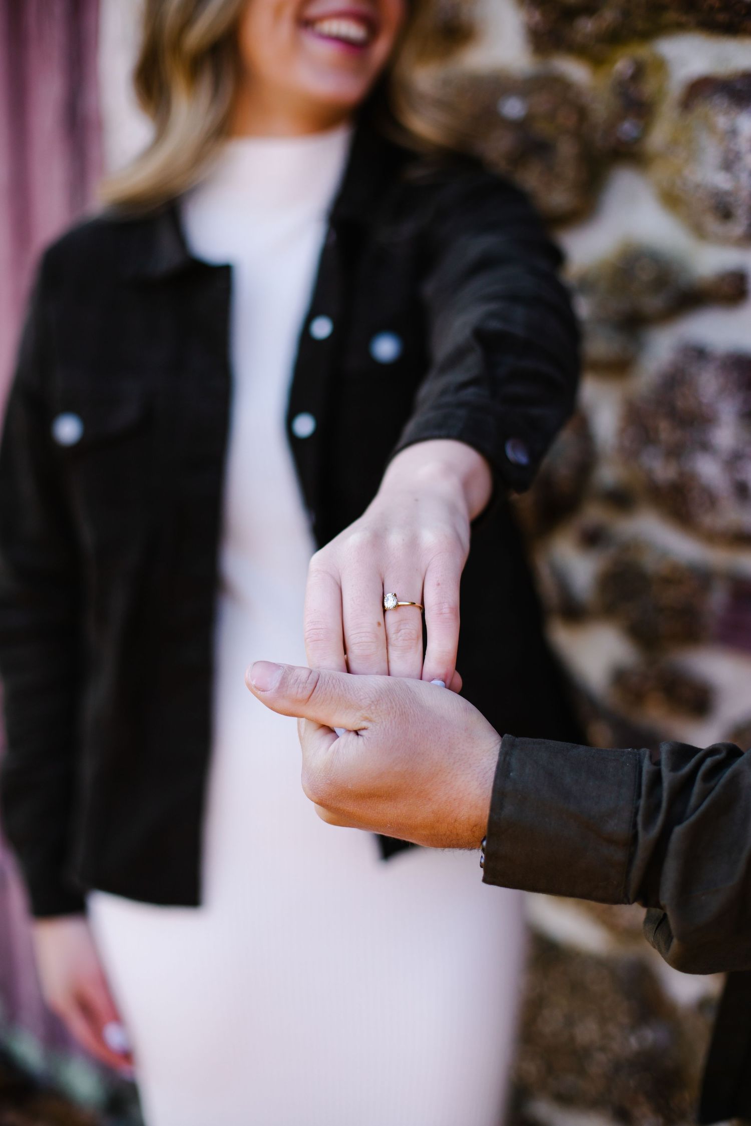 Close-up of woman extending hand to show diamond engagement ring while man holds it gently.