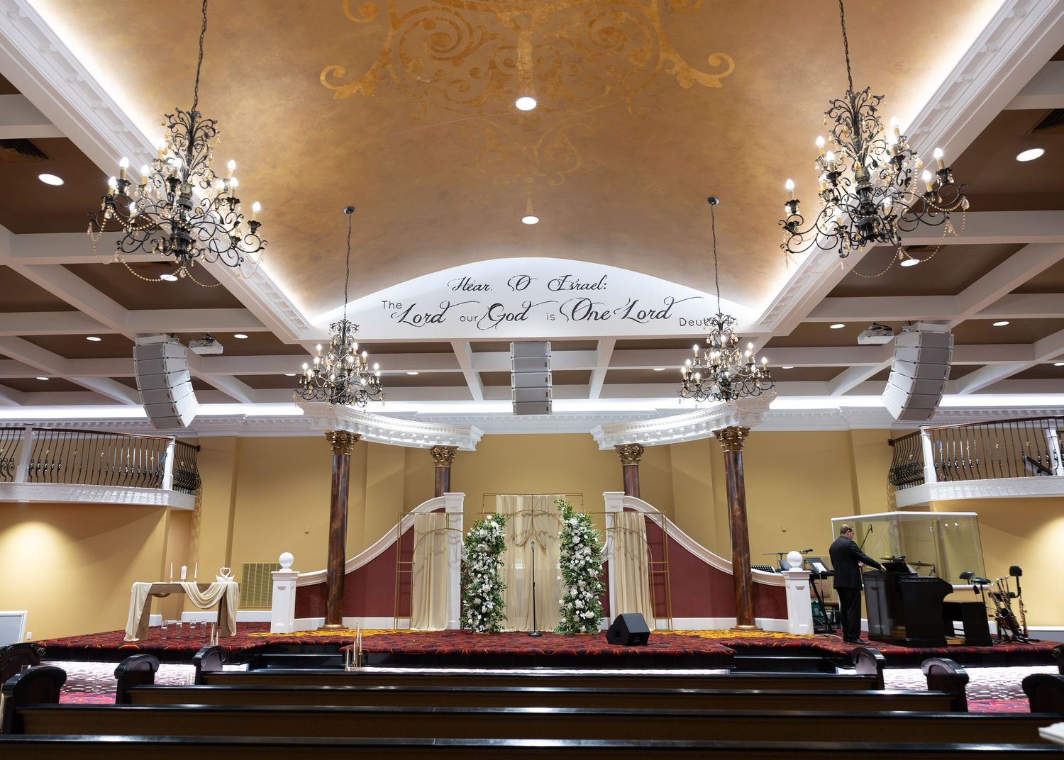 Elegant church wedding ceremony venue with chandeliers, floral arrangements, and scripture text on the arched ceiling.