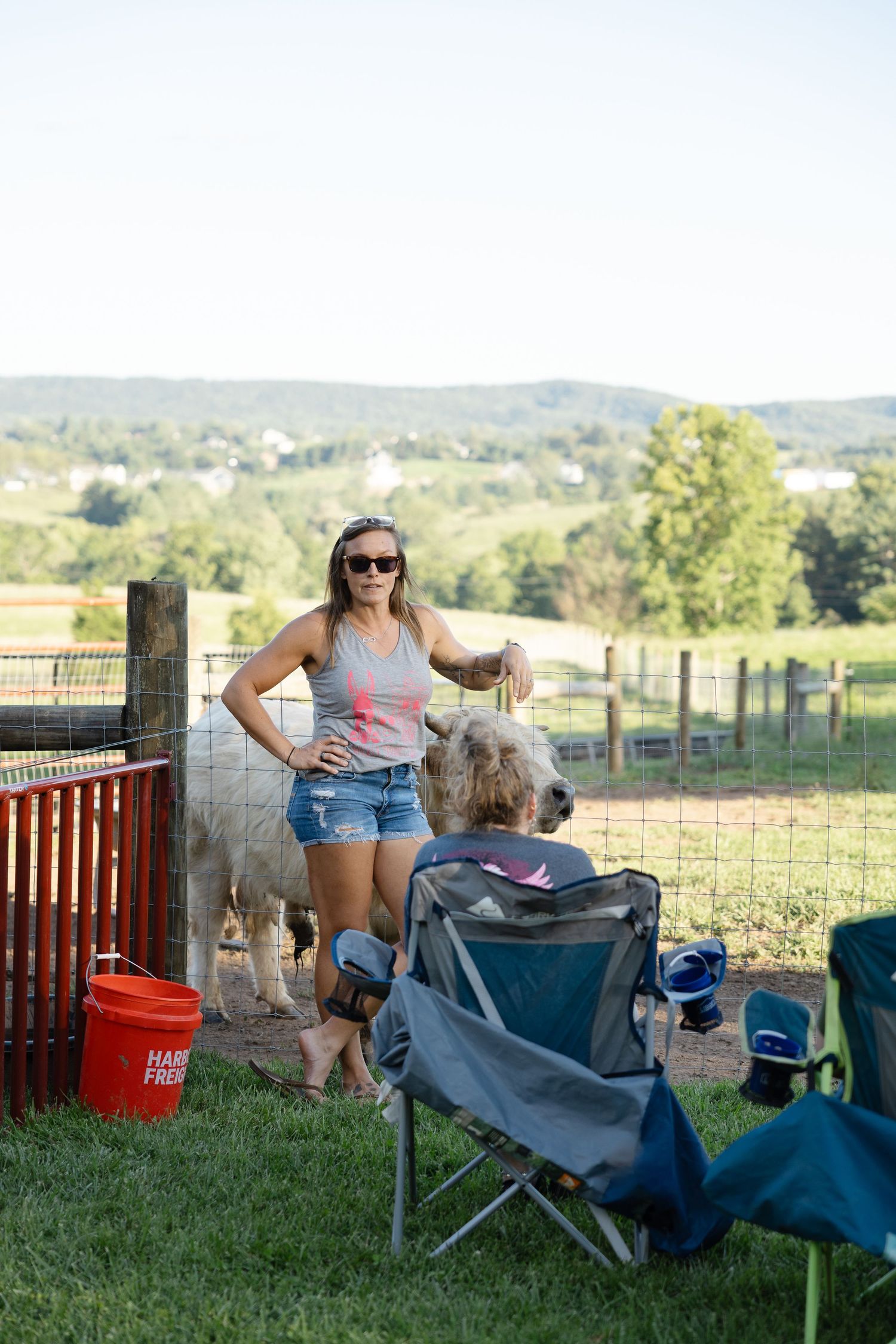 Woman in sunglasses and denim shorts petting a white llama at a farm animal encounter event.