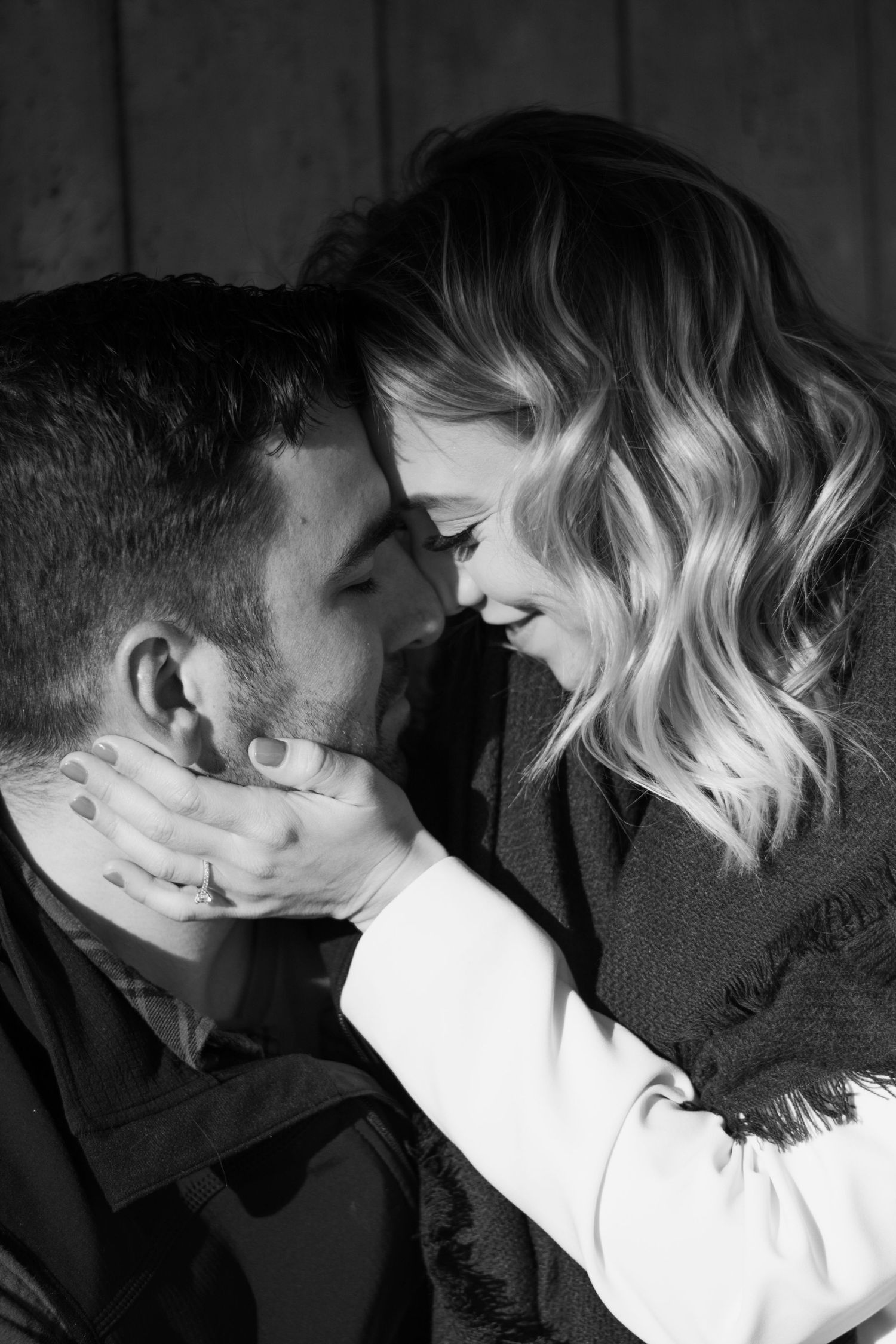 Black and white photo of a romantic couple touching foreheads and smiling, the woman gently holding the mans face.