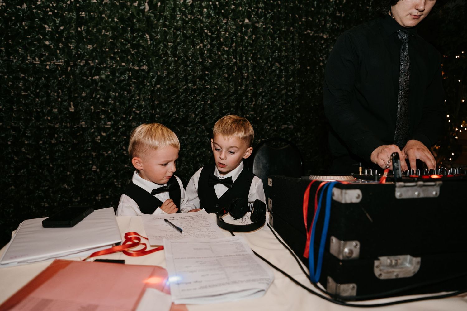 Two young boys in bow ties watching DJ equipment at a wedding reception.