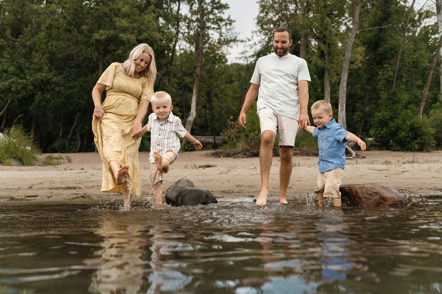 A happy family with two toddlers splashes in shallow water on a sandy beach.