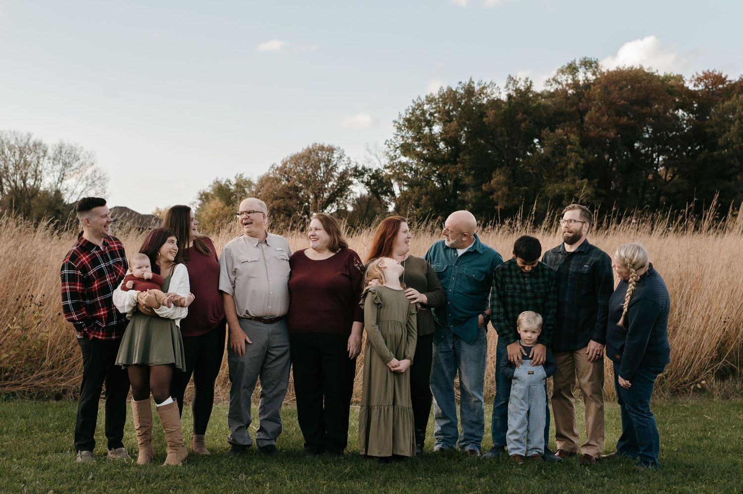 An extended multigenerational family stands together in a scenic autumn field near tall grasses. Woodbury, Minnesota.