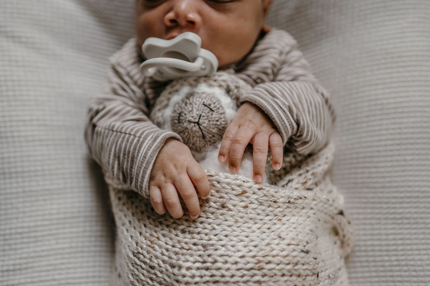 A sleeping newborn in a knit wrap holds a stuffed bunny with a pacifier.