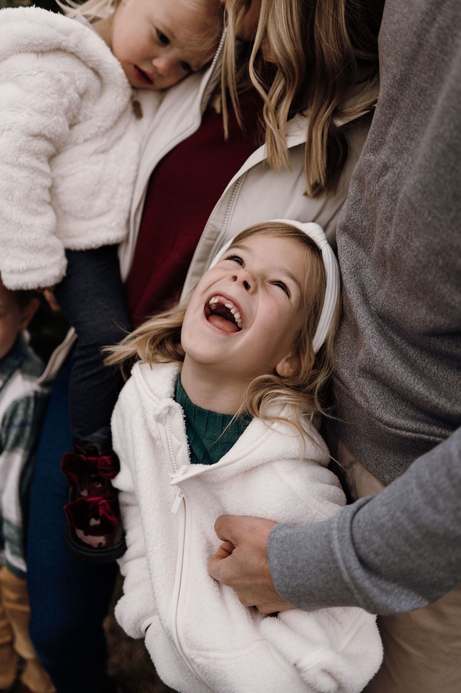 Joyful blonde child laughing brightly while standing between parents during family photo session. Lake Elmo, Minnesota.