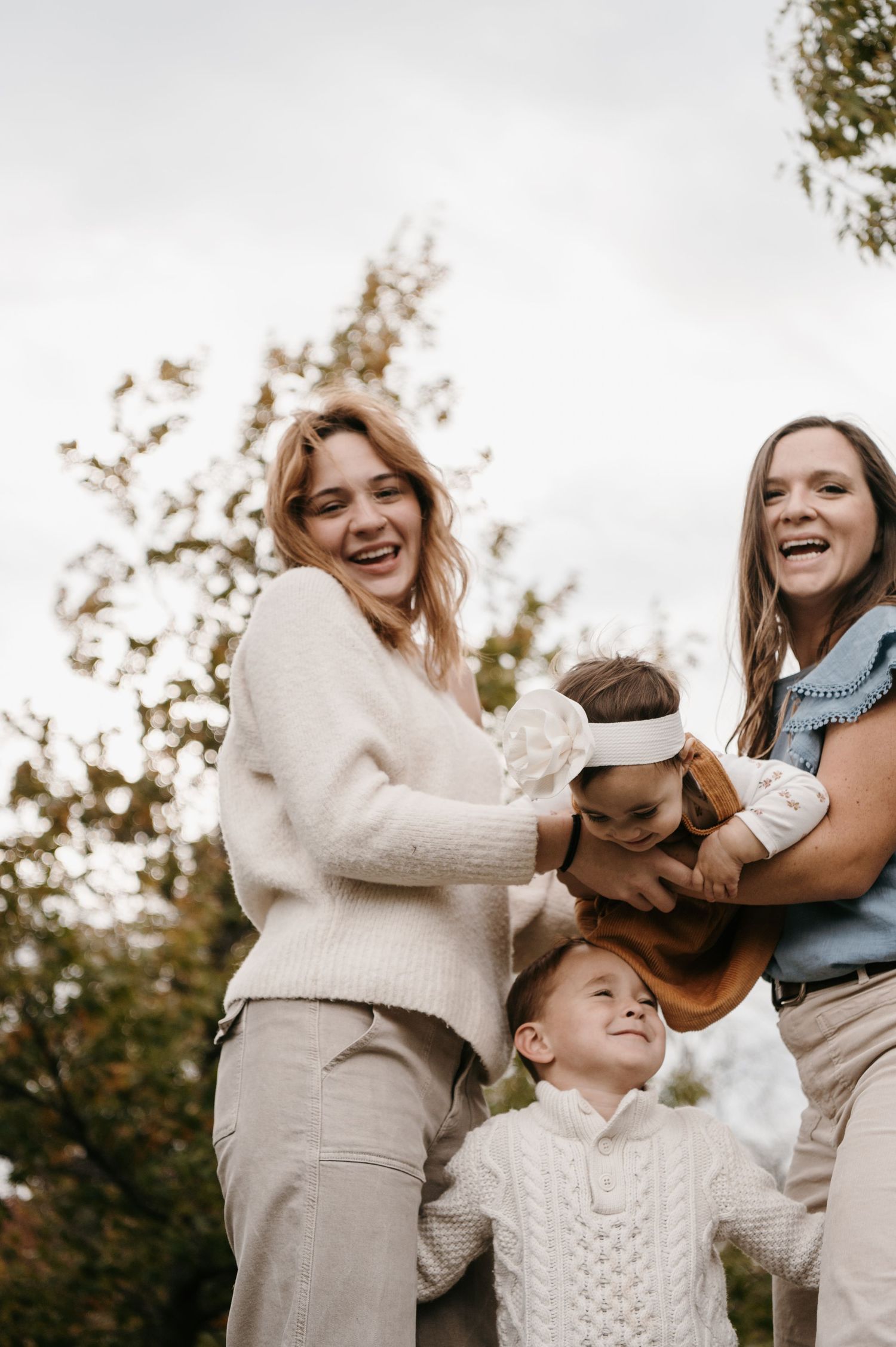 Two laughing women play with two young children outdoors on an overcast fall day. Woodbury, Minnesota.
