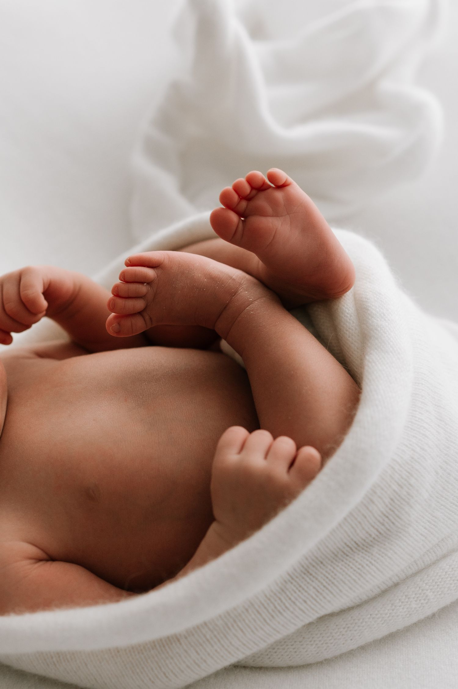 Close-up of a newborn baby wrapped in a soft white blanket showing tiny feet and hands. Fresh 48 hospital photos.