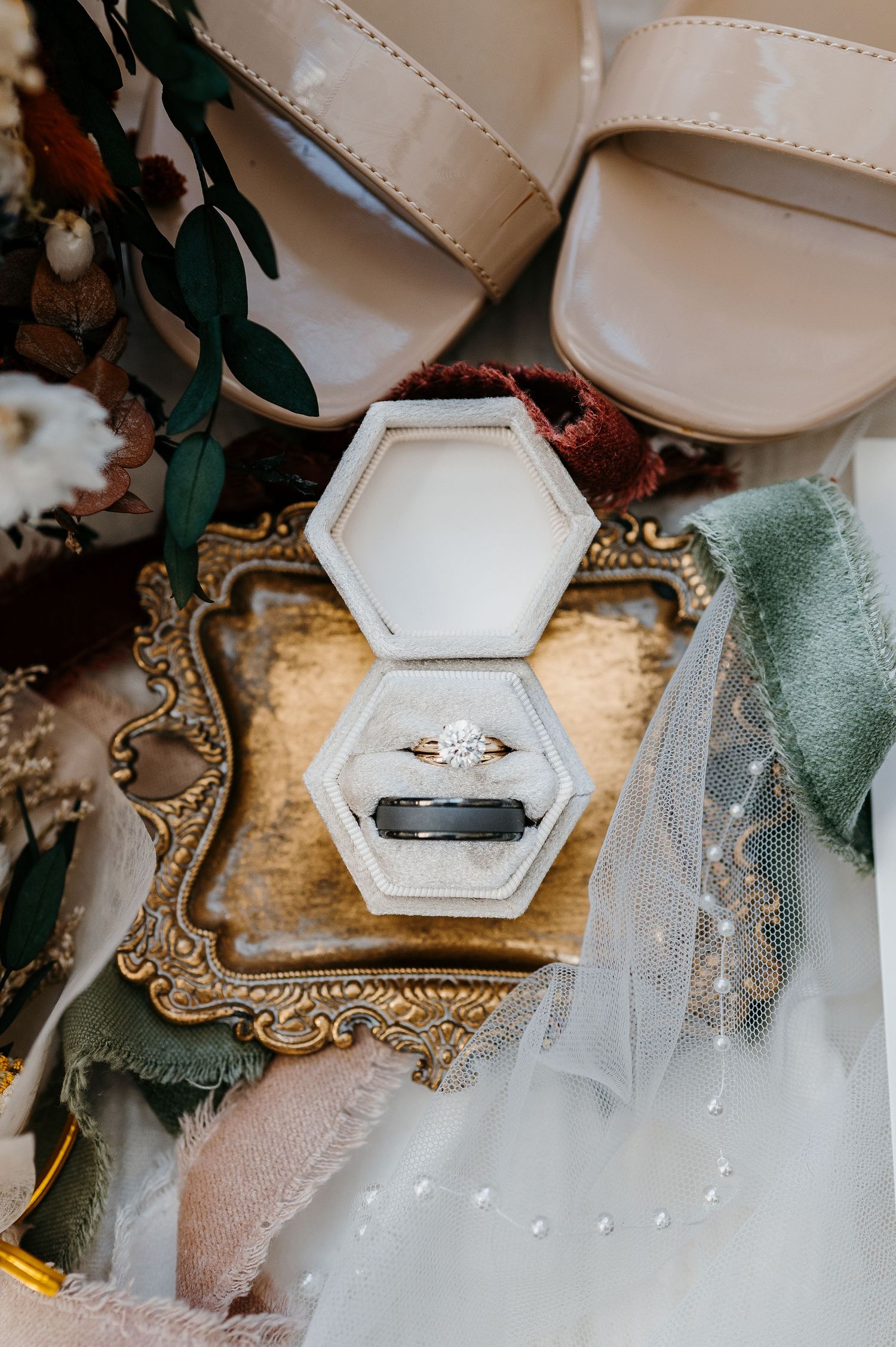 Diamond engagement ring and black wedding band in hexagon velvet box on vintage tray.