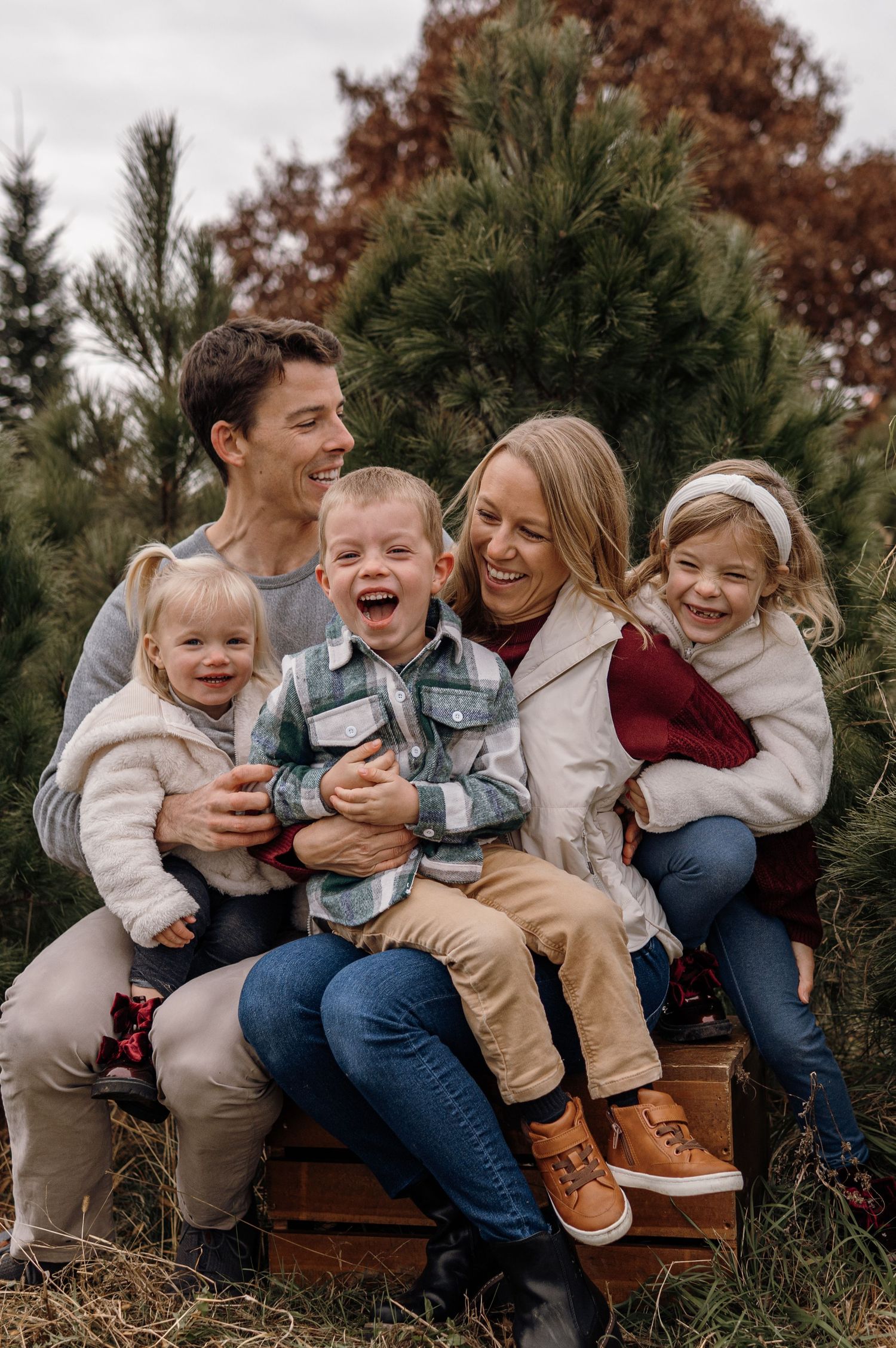 A joyful family of five laughs together at a Christmas tree farm on a cloudy autumn day.