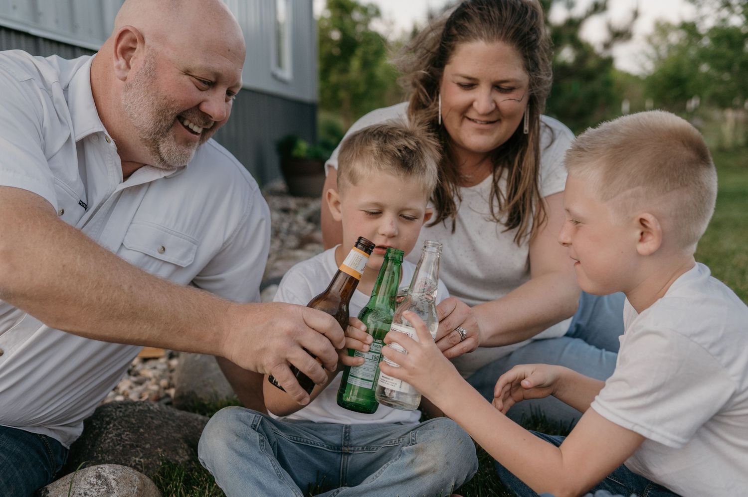 Grandparents and two young boys cheerfully clinking beer bottles together outdoors in backyard. Home, Wisconsin,