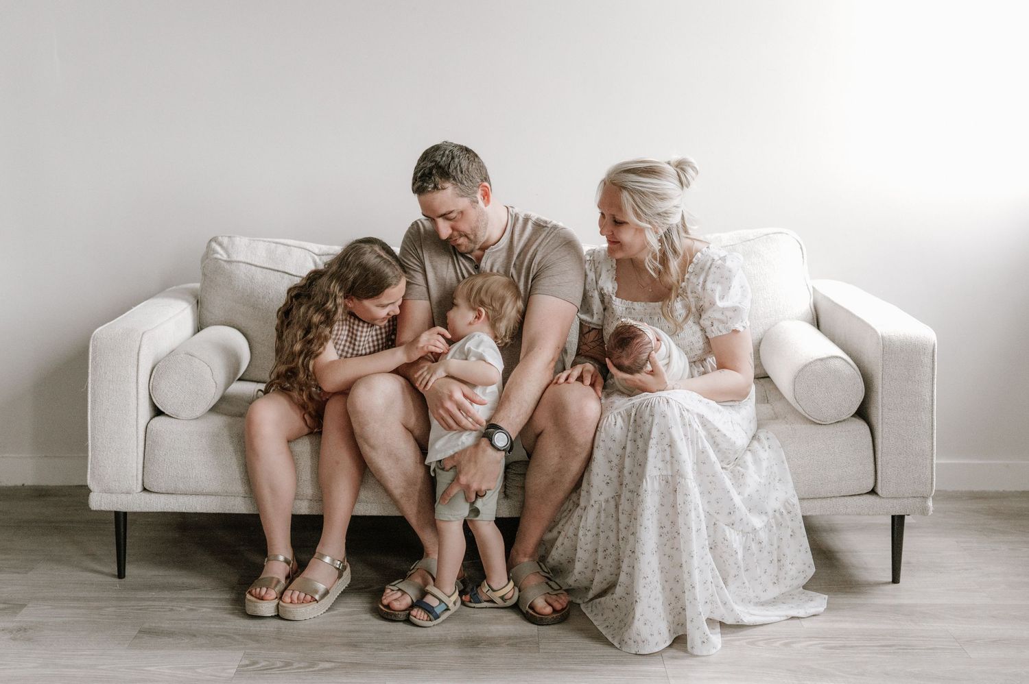 Family with two children and newborn twins sitting together on white couch at home.