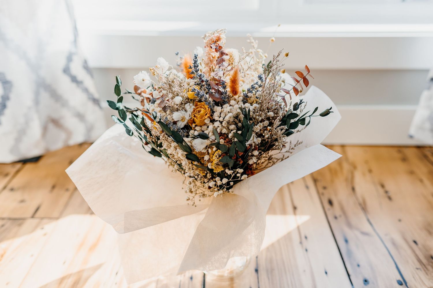 Rustic dried flower bouquet wrapped in white tissue paper on a wooden floor.