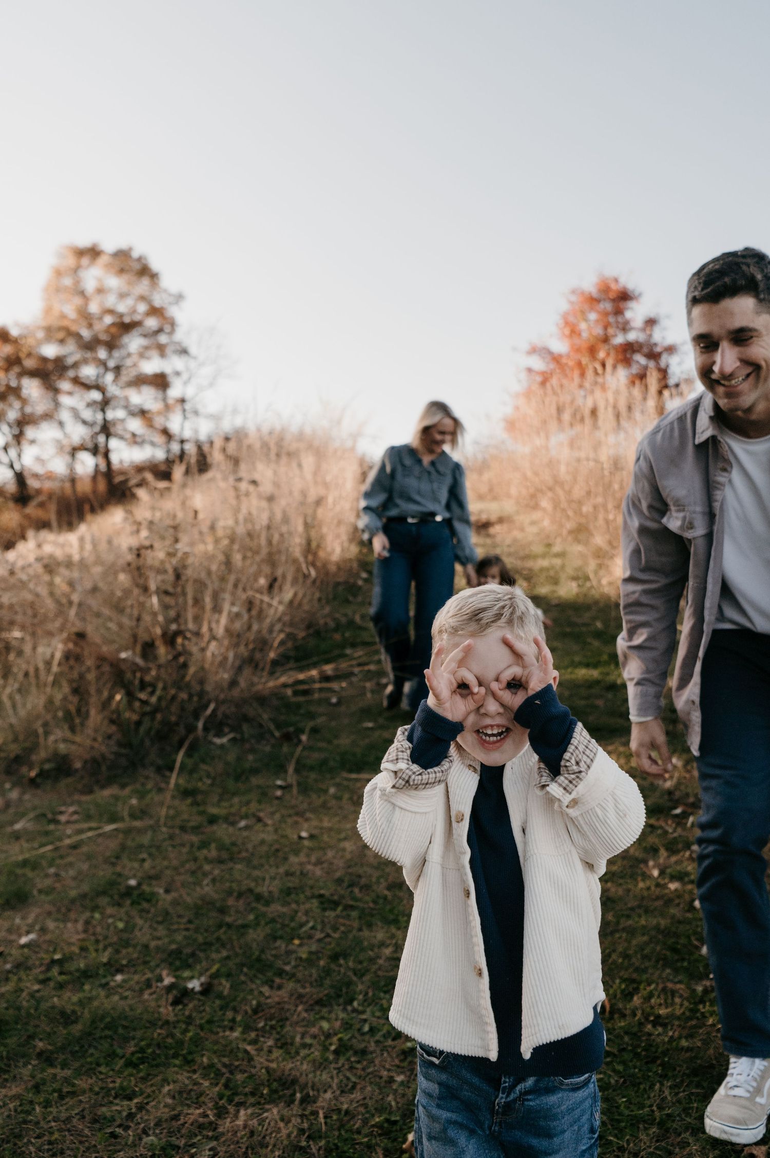 Young boy making silly binocular gestures with hands during outdoor family photo session. Hudson, Wisconsin.