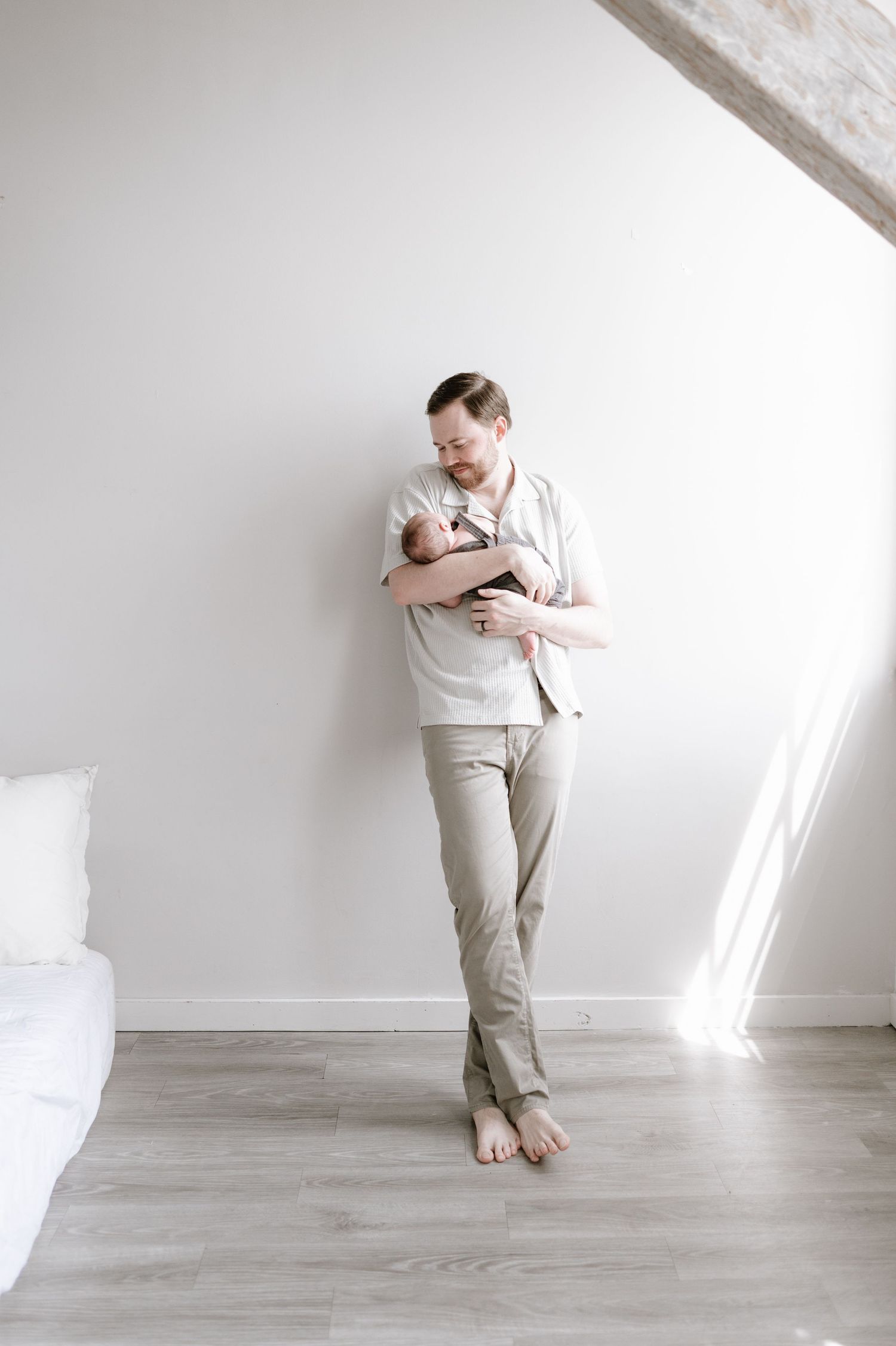 Father holding newborn baby against white wall in minimalist nursery room.